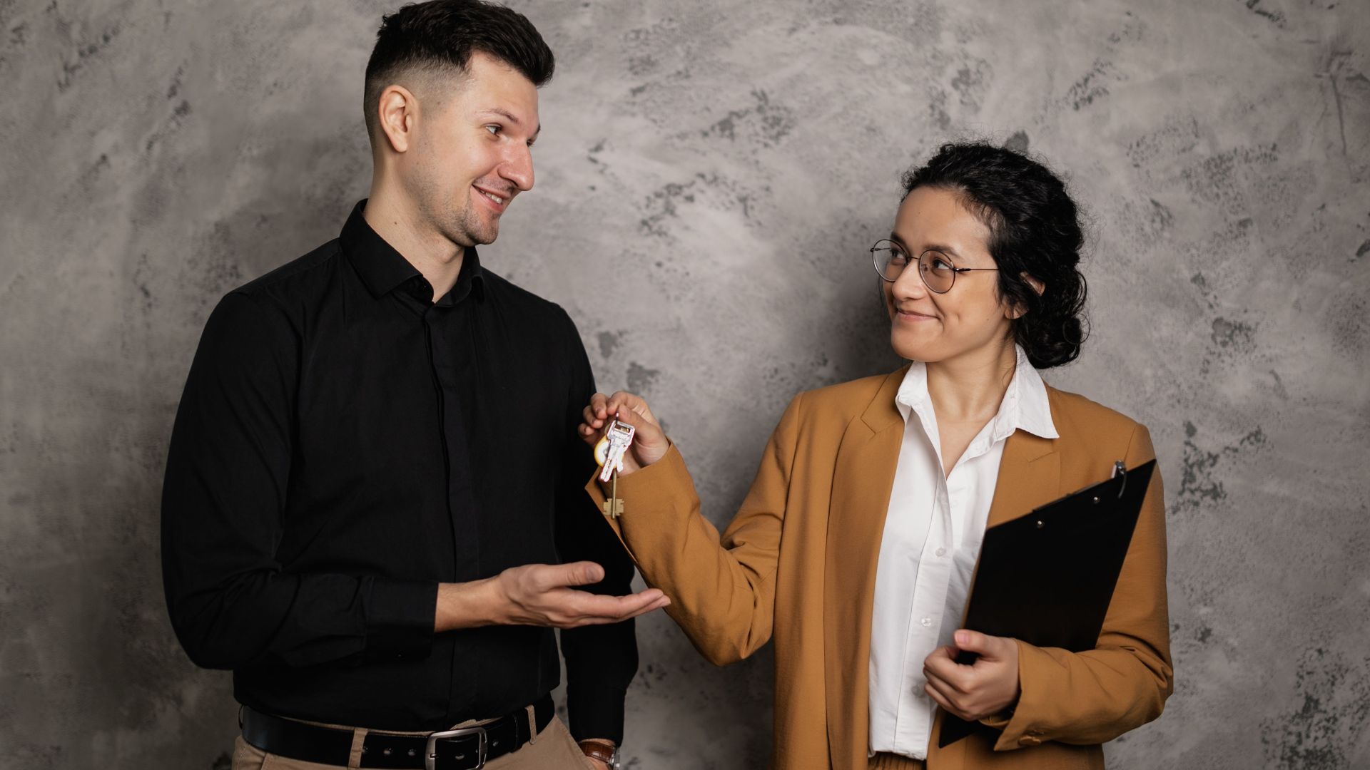 A real estate agent smiling as they hand over house keys to a new homeowner in an indoor setting.
