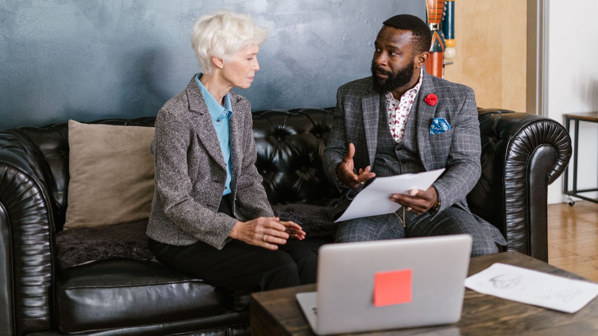 Two professionals engaged in a productive business discussion, seated on a leather couch in an office environment.