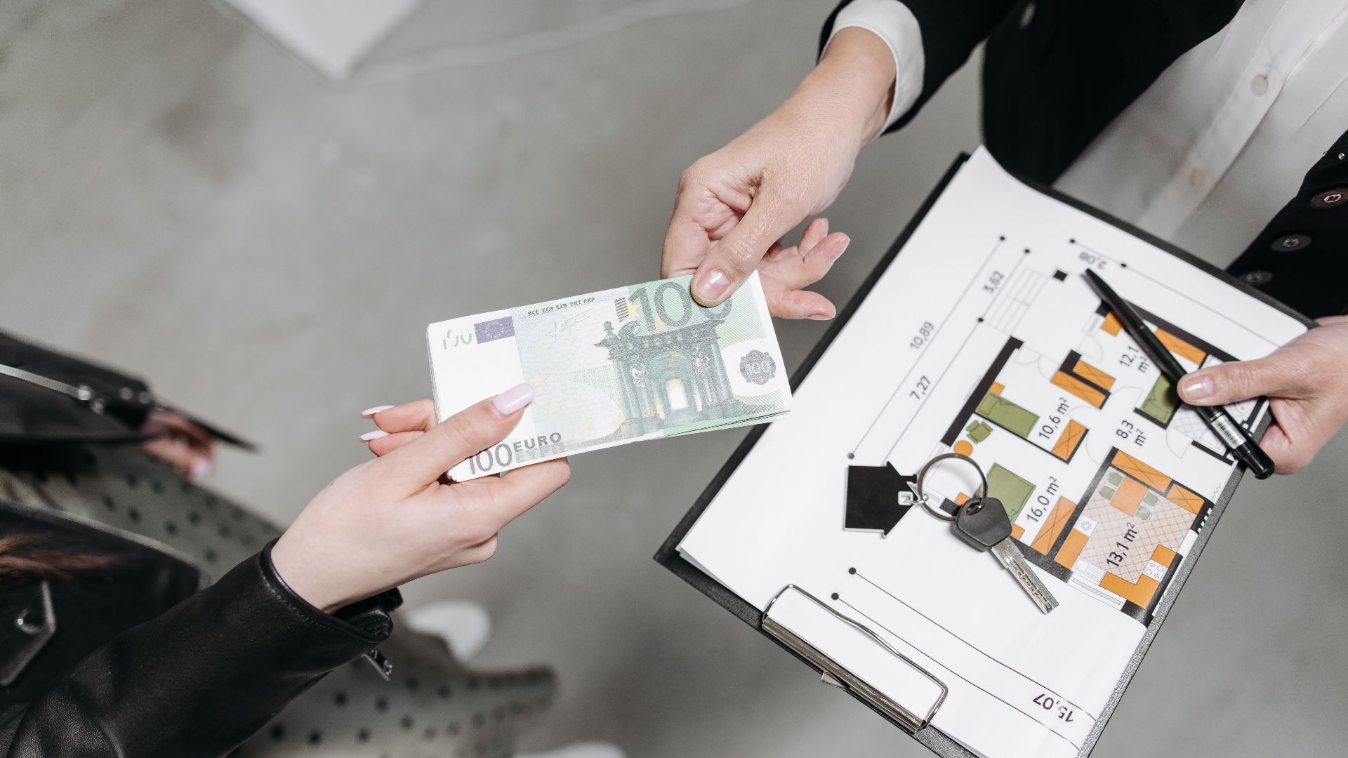 Close-up of a real estate transaction with euro bill, keys, and floor plan.