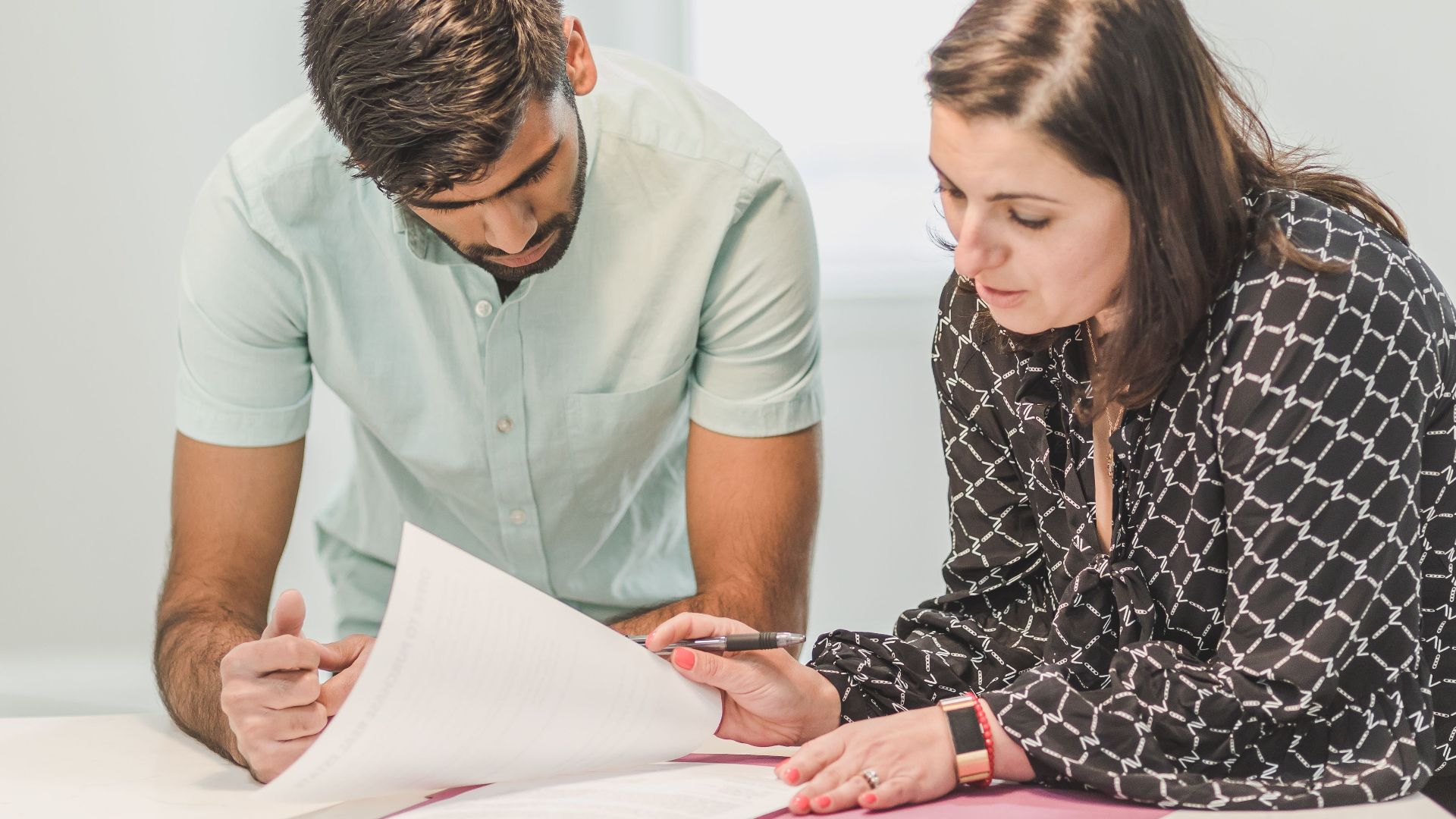 Real estate agent assisting first-time homebuyer with documents inside a bright room.