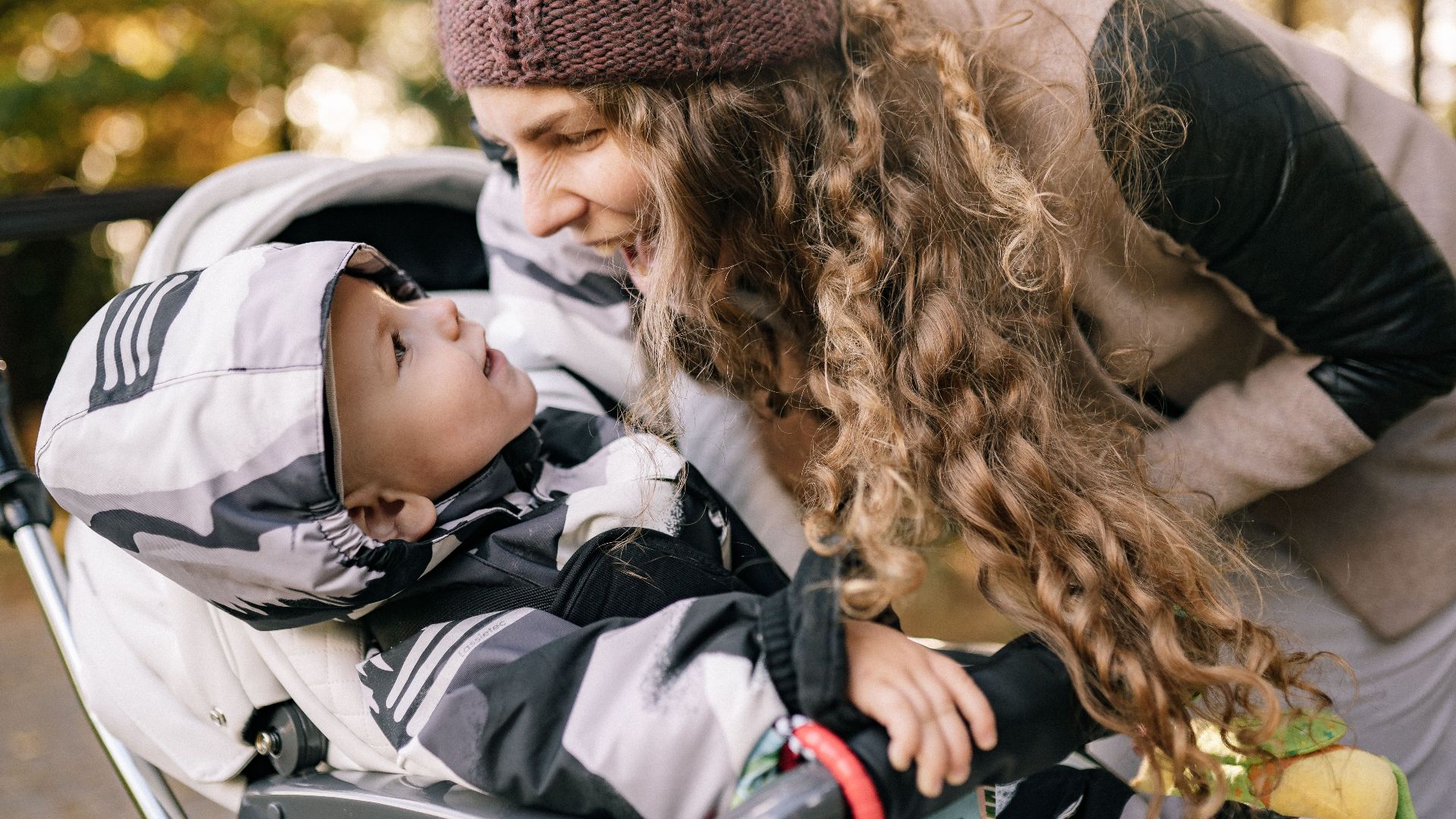 A joyful mother engaging with her baby in a stroller during a sunny day stroll.