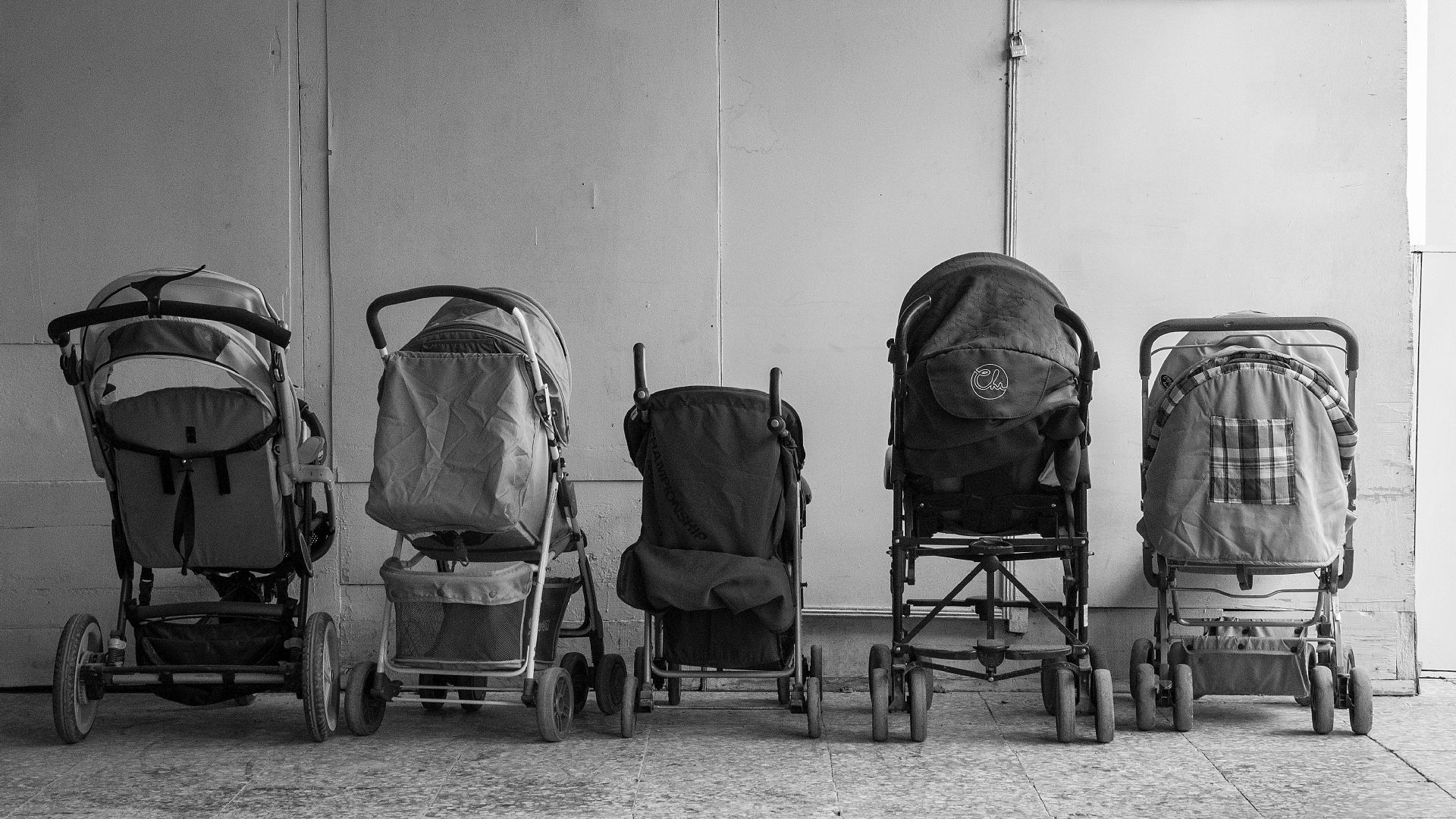 Old baby carriages placed in row near wall in hallway of aged residential building