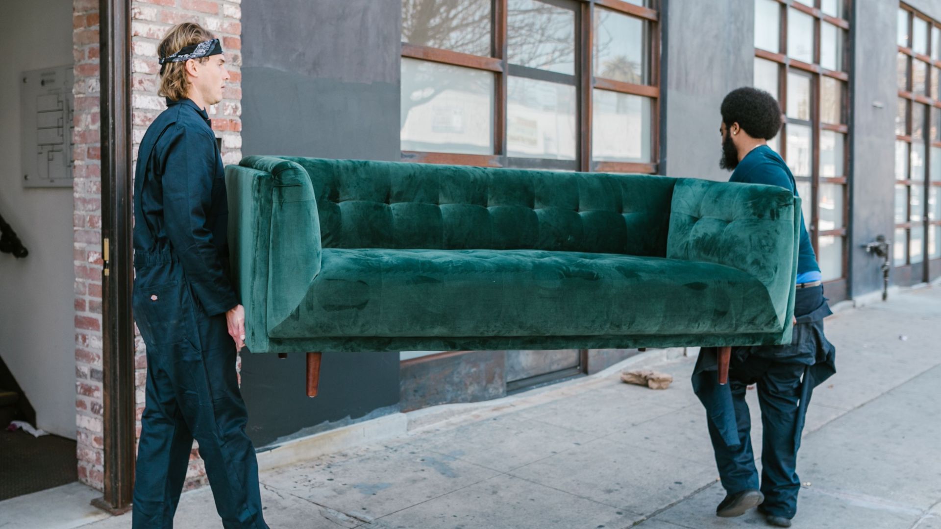 Two men carrying a green sofa on a city street, showcasing teamwork and moving services.
