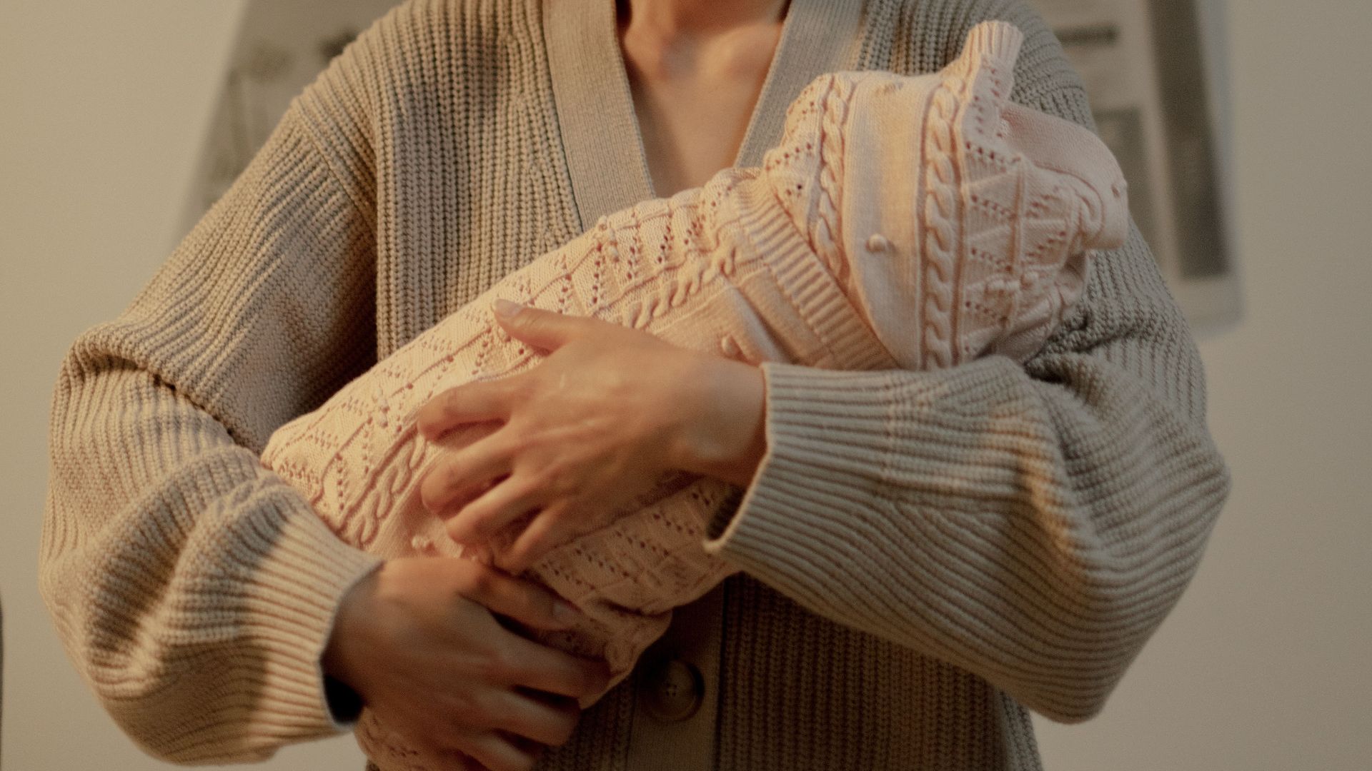 A mother holds her newborn baby indoors, surrounded by newspapers, conveying a thoughtful expression.