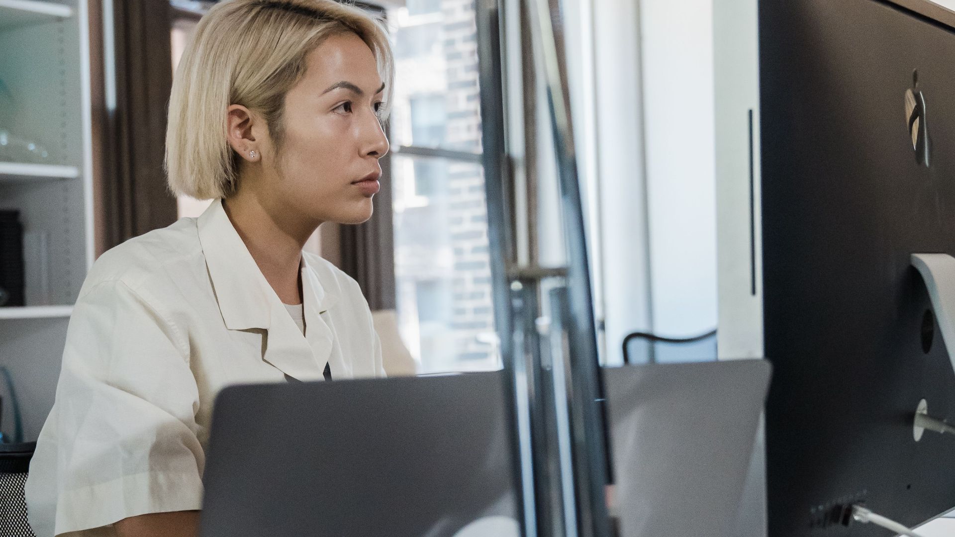 Blonde woman working on a computer and laptop at an office desk with modern workspace.