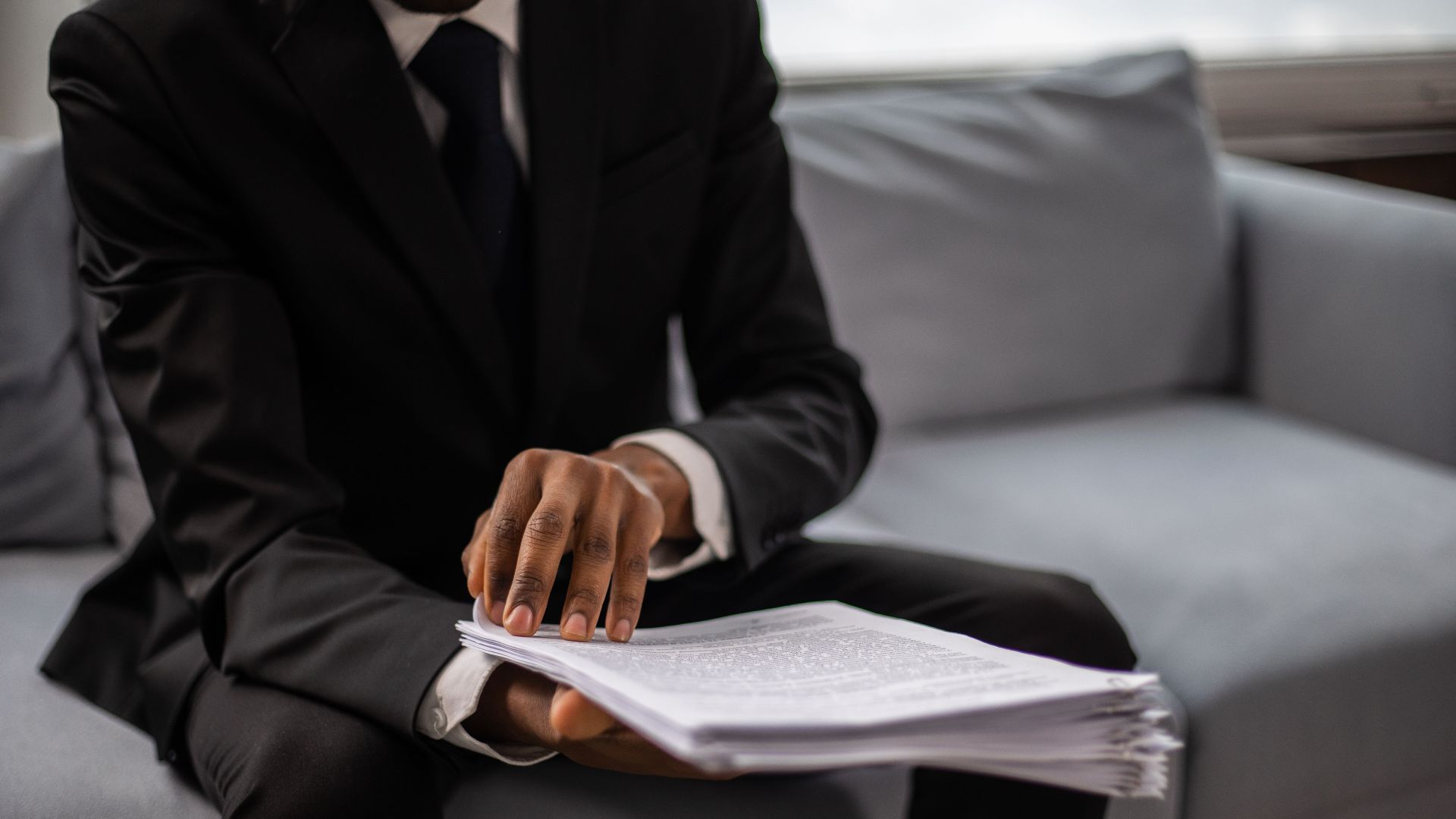 Close-up of a businessman in a suit reviewing documents while seated on a sofa indoors.