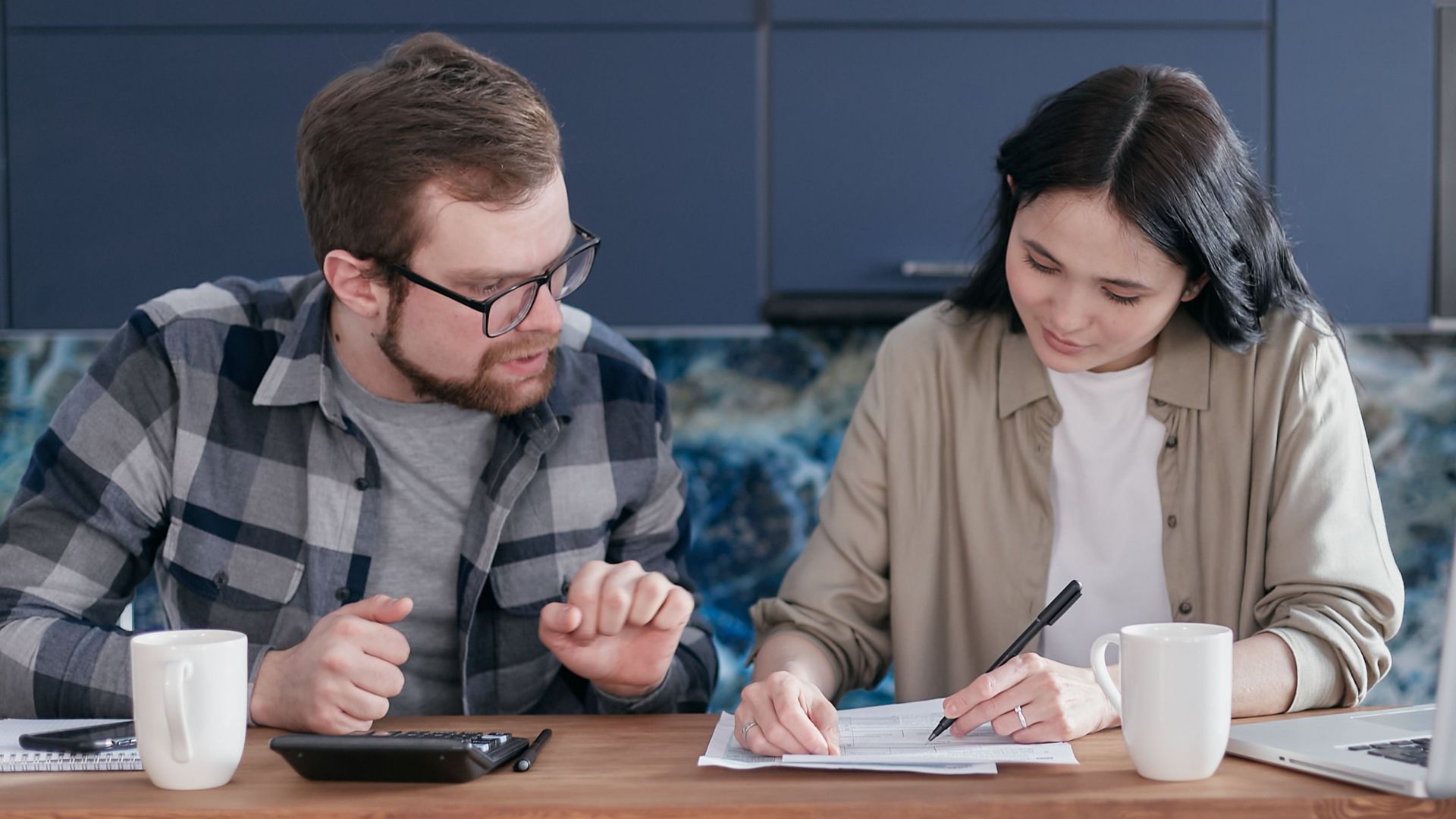A couple sitting at a table managing their finances with a laptop and calculator, appearing focused.