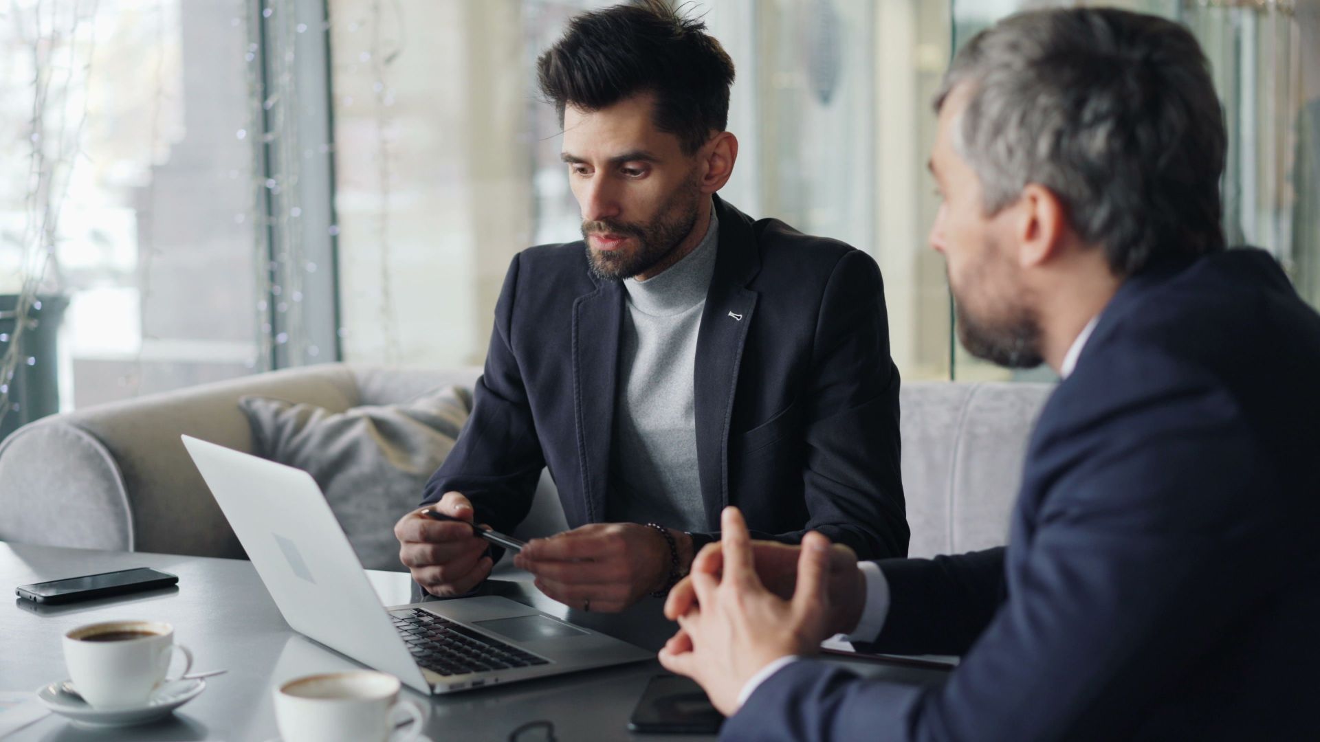 Two businessmen engaged in a meeting in a cozy café, discussing on a laptop.