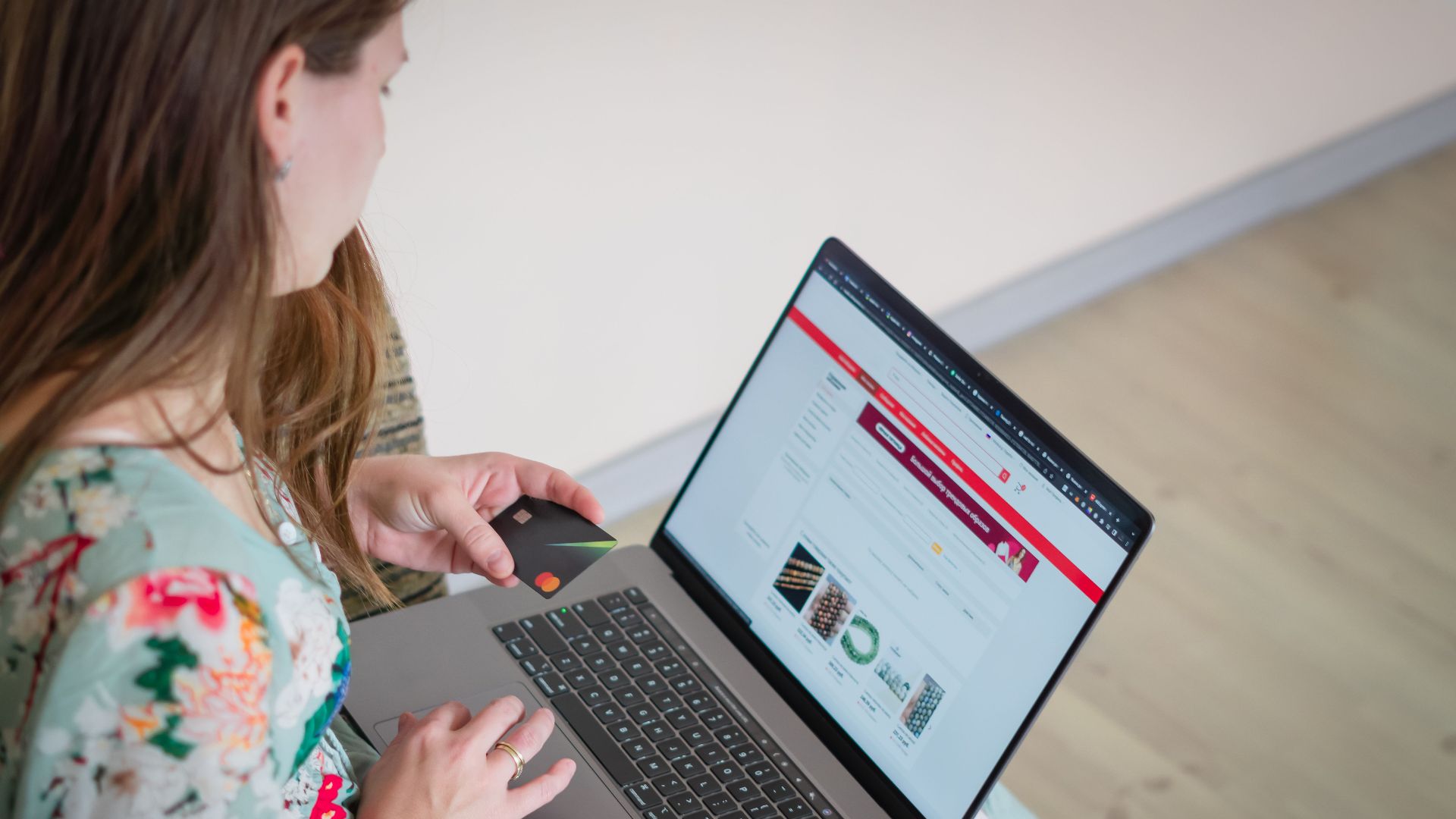 Woman in floral dress shopping online with a laptop and credit card indoors.