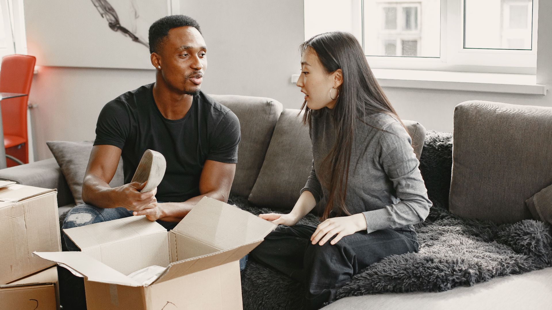 Interracial couple unboxing items on a sofa at home, showcasing excitement and conversation.