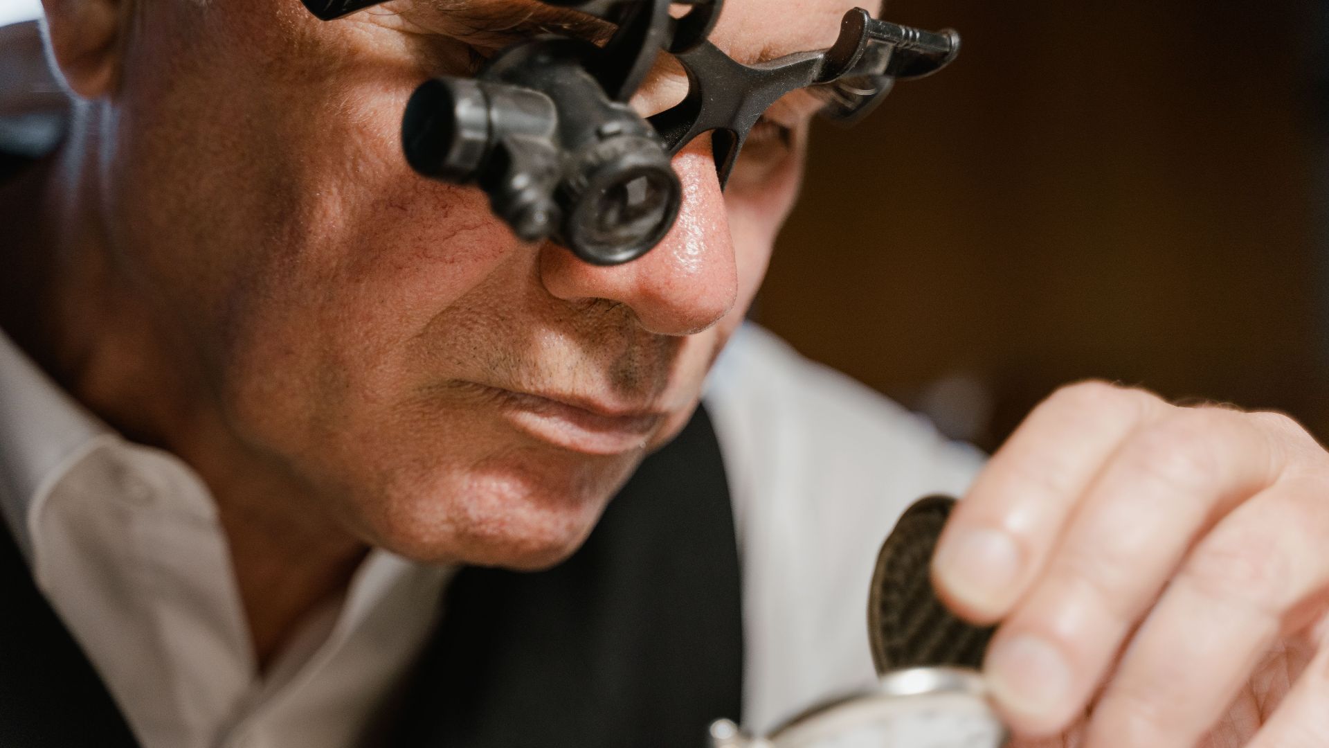 Watchmaker inspects pocket watch using loupe in close-up scene.