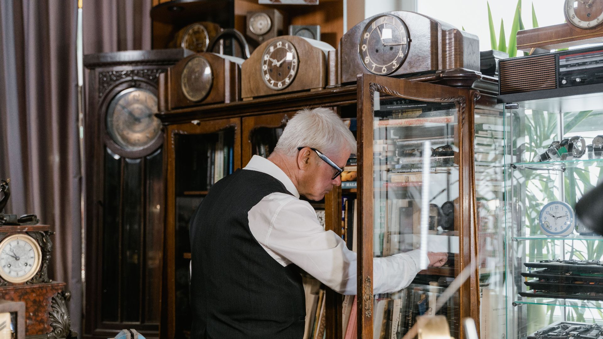 An older man examines clocks in a vintage shop filled with antique timepieces.