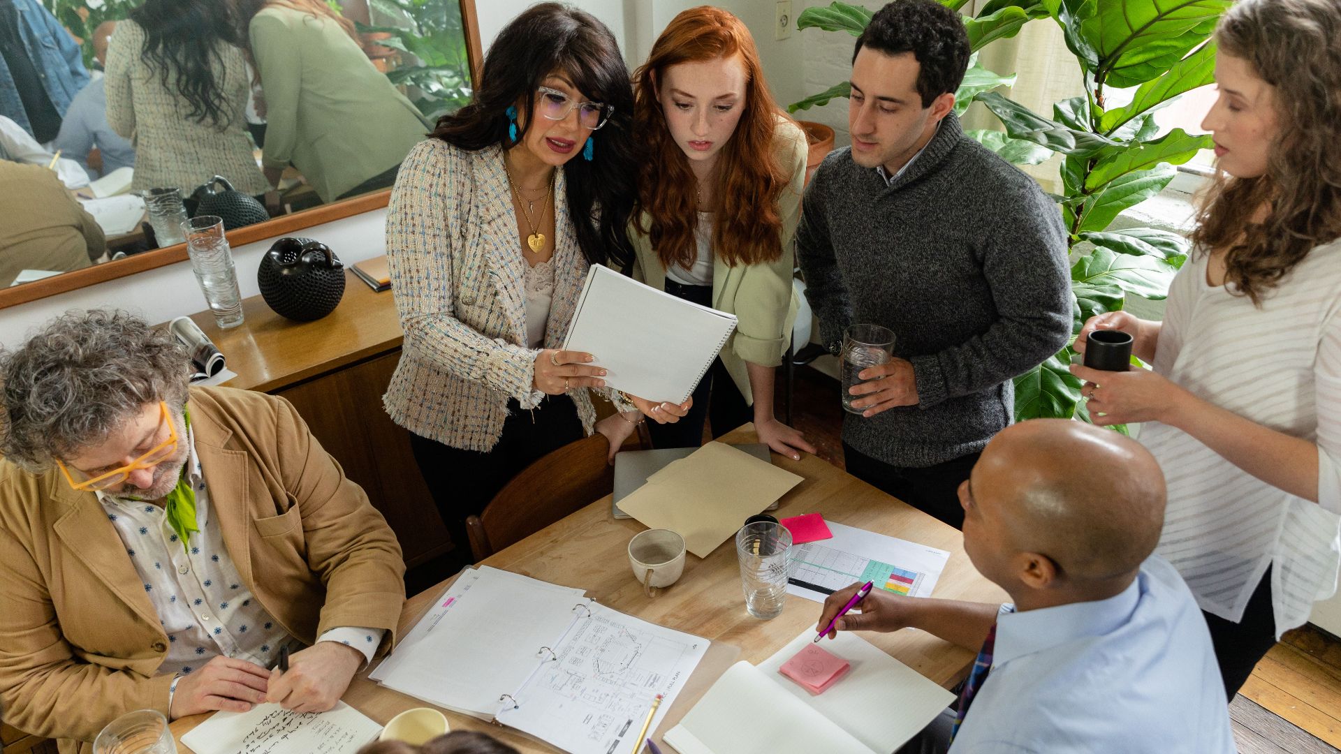 A diverse team discusses documents around a table in a modern office setting, promoting teamwork and collaboration.