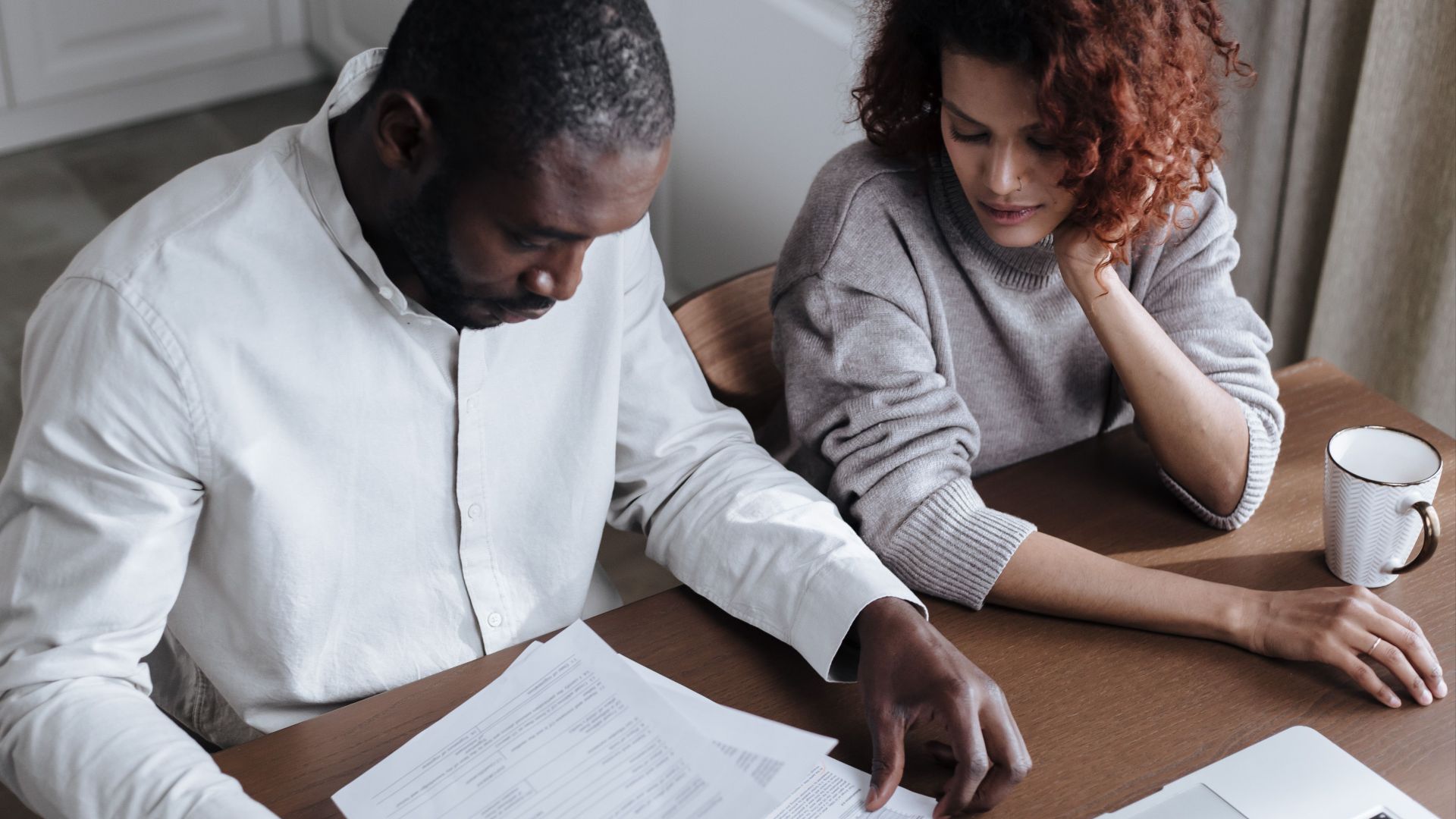 A couple reviews important documents together at a home desk with a laptop.