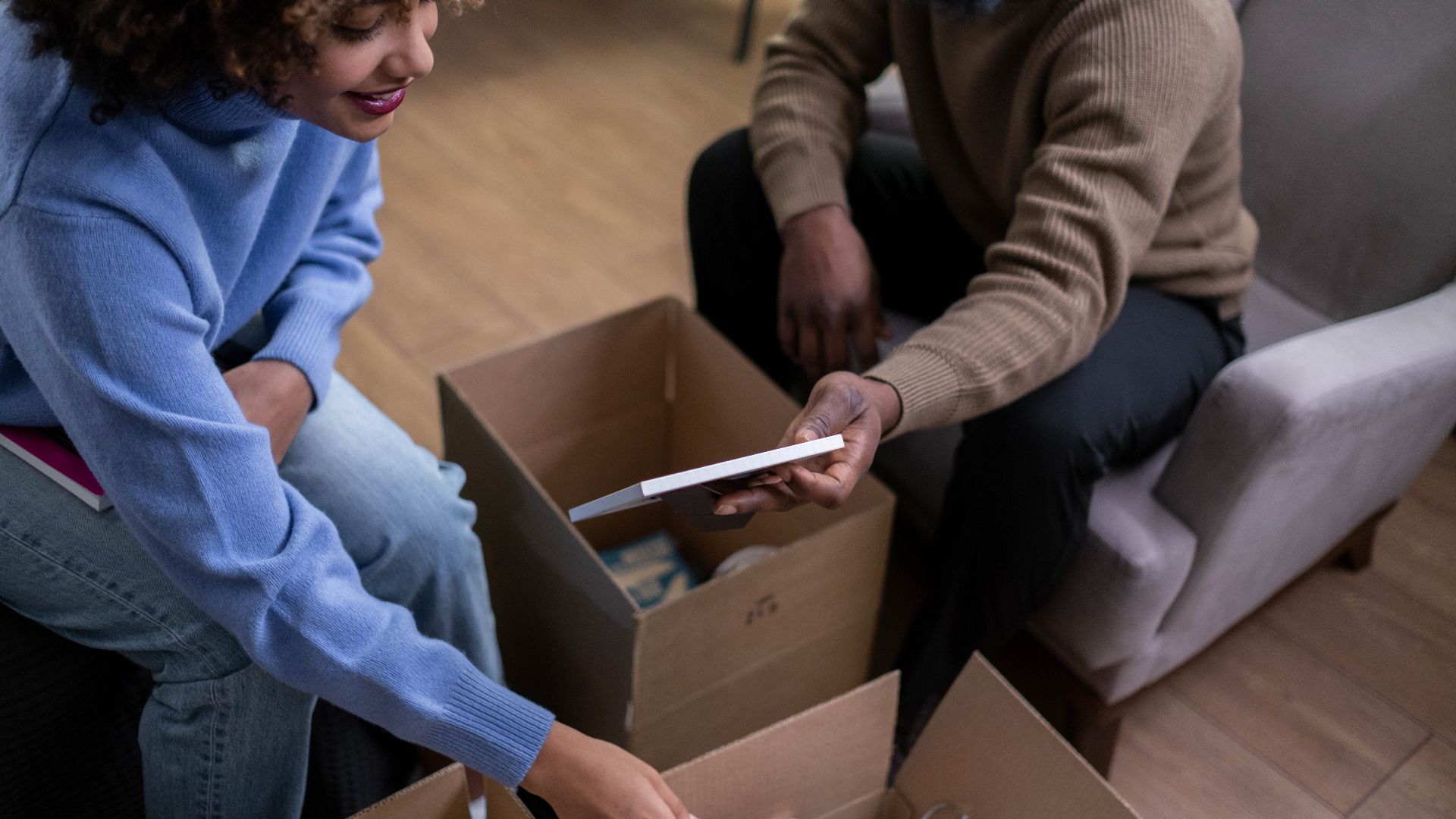A couple sorts through boxes, packing and organizing household items together indoors.