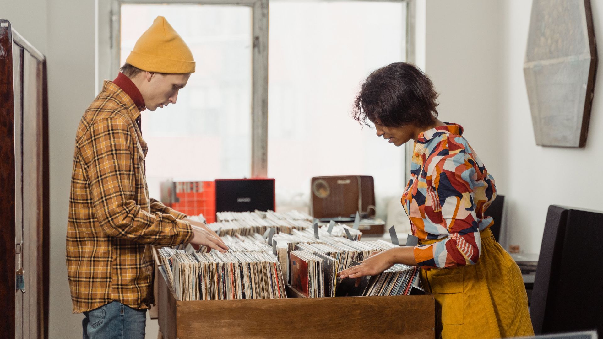 A young man and woman browsing a vinyl record collection in a vintage store setting indoors.