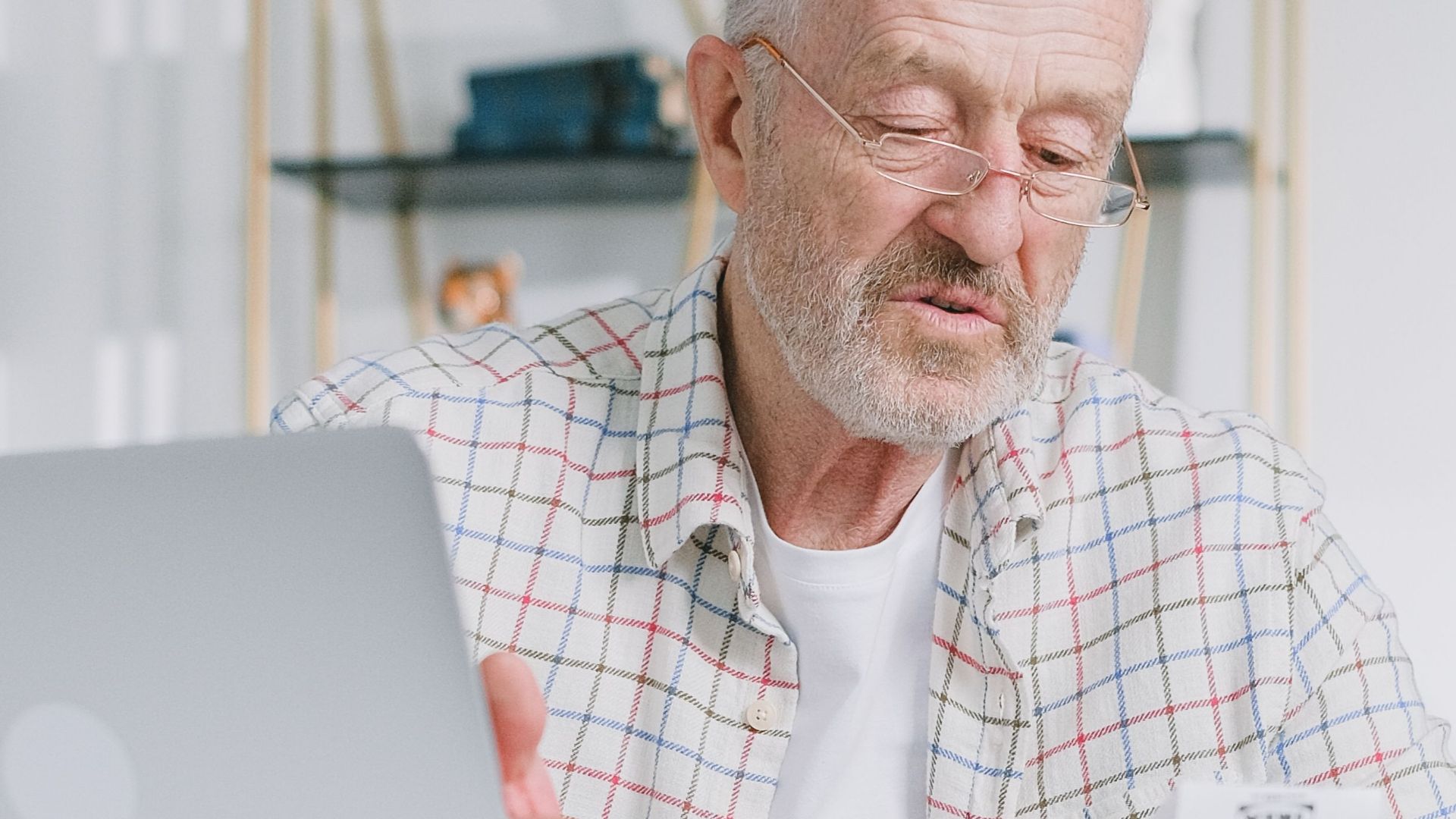 Elderly man reading papers at home with a laptop, emphasizing financial planning.