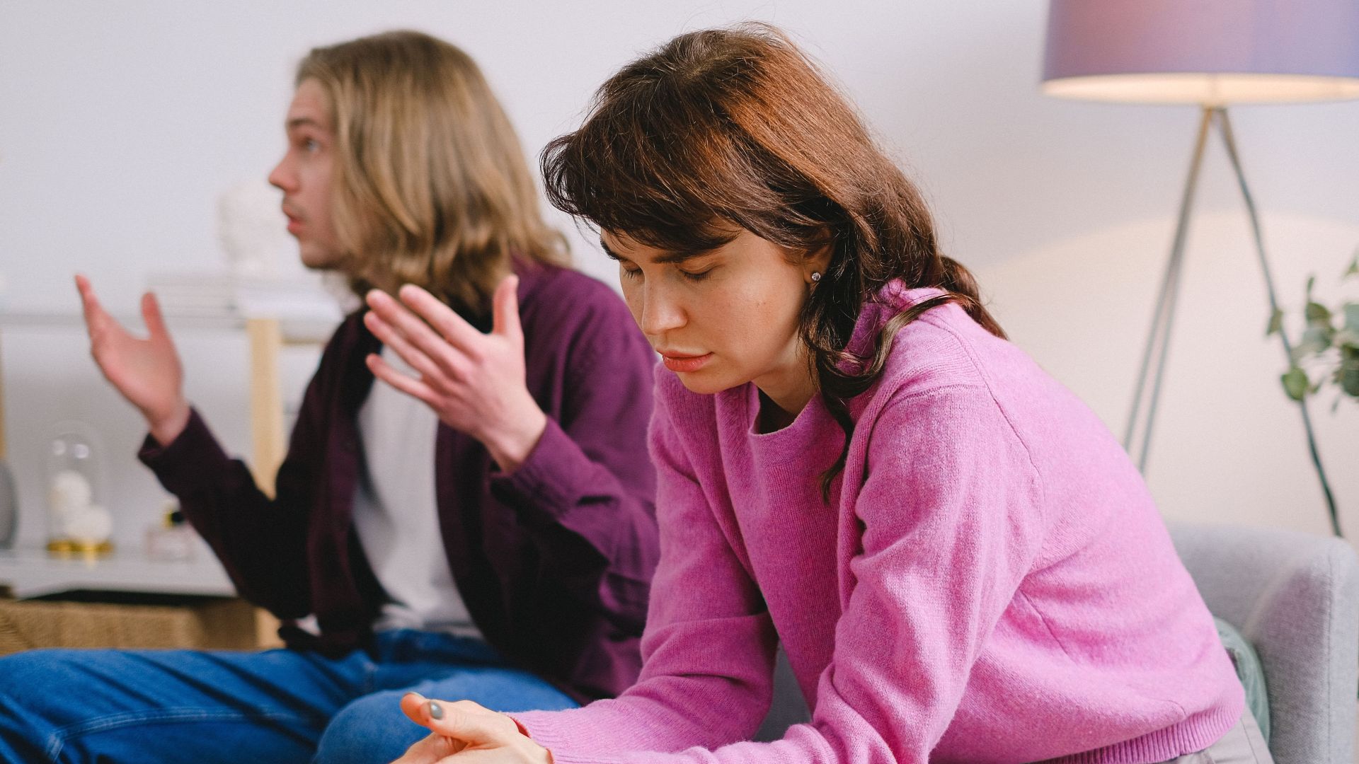 A couple having a serious discussion indoors; one looks upset while the other gestures expressively.