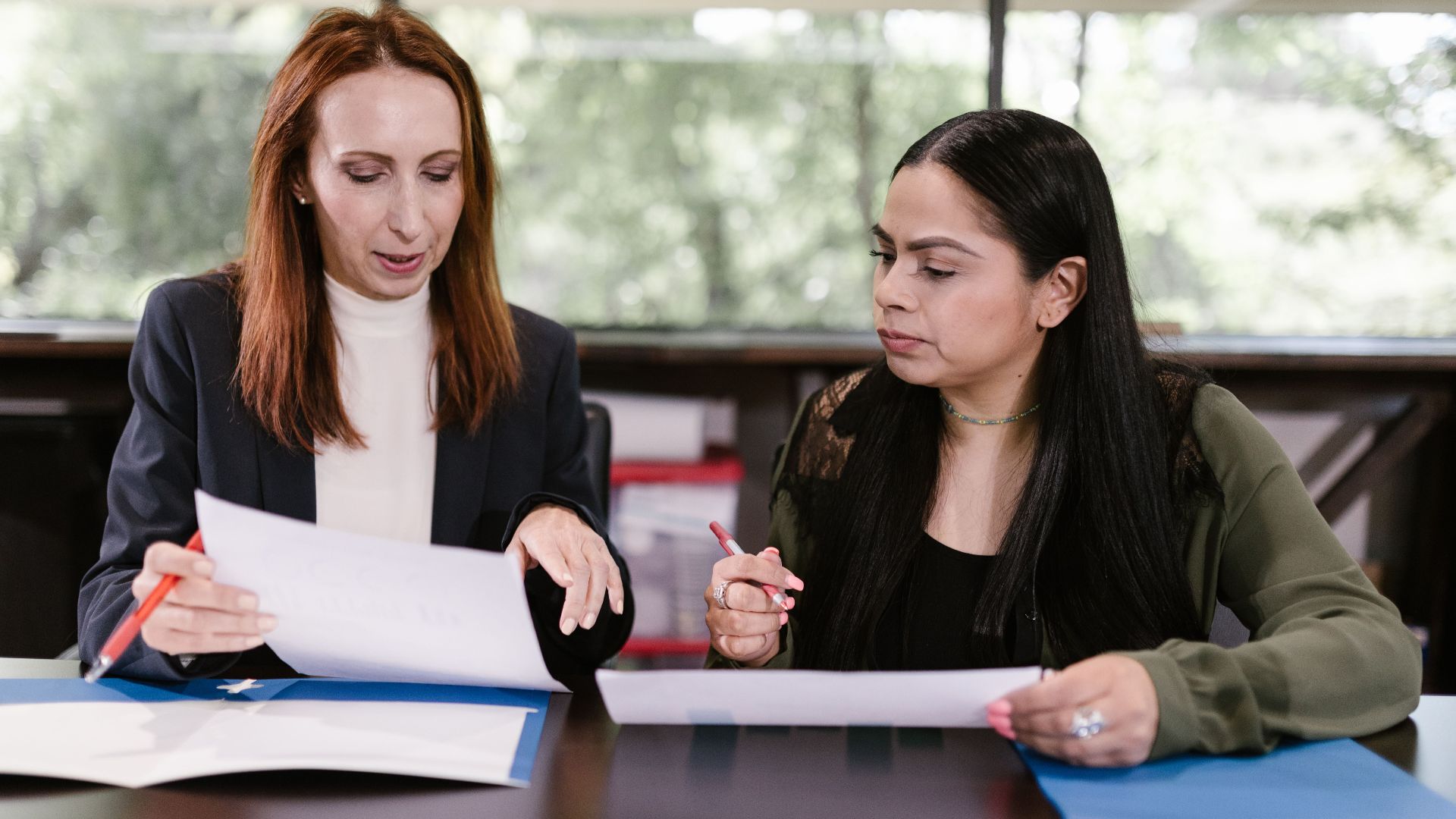 Two professional women reviewing documents in a well-lit office setting.