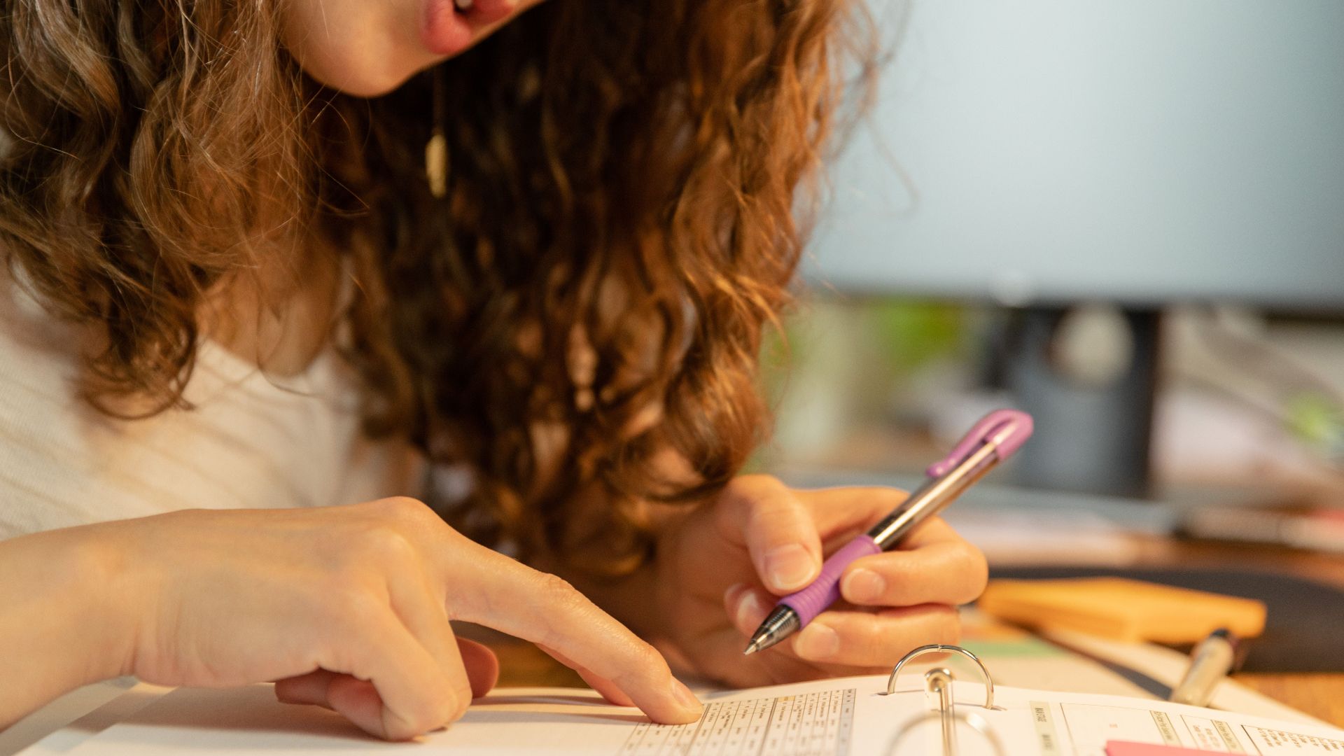 Focused woman pointing and writing on paper in binder with a purple pen.