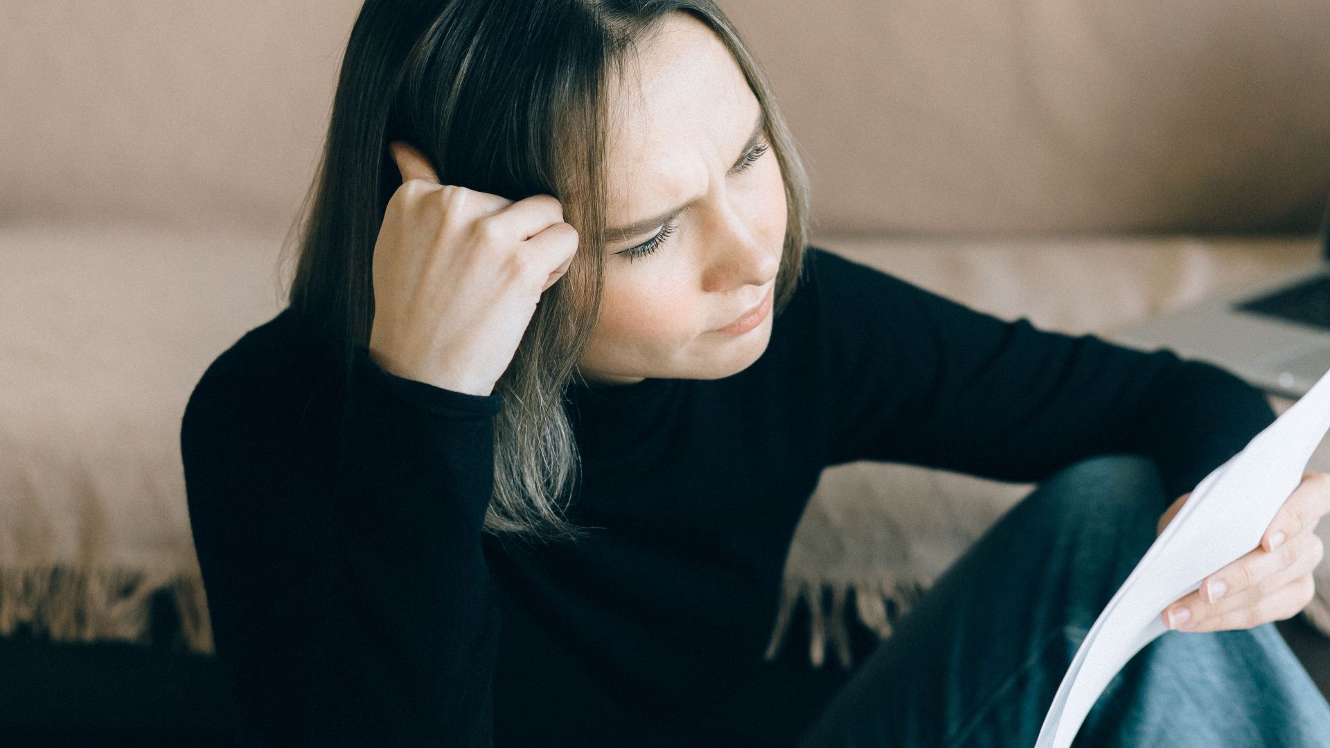 Focused woman analyzing papers with a laptop open, symbolizing thoughtful consideration.