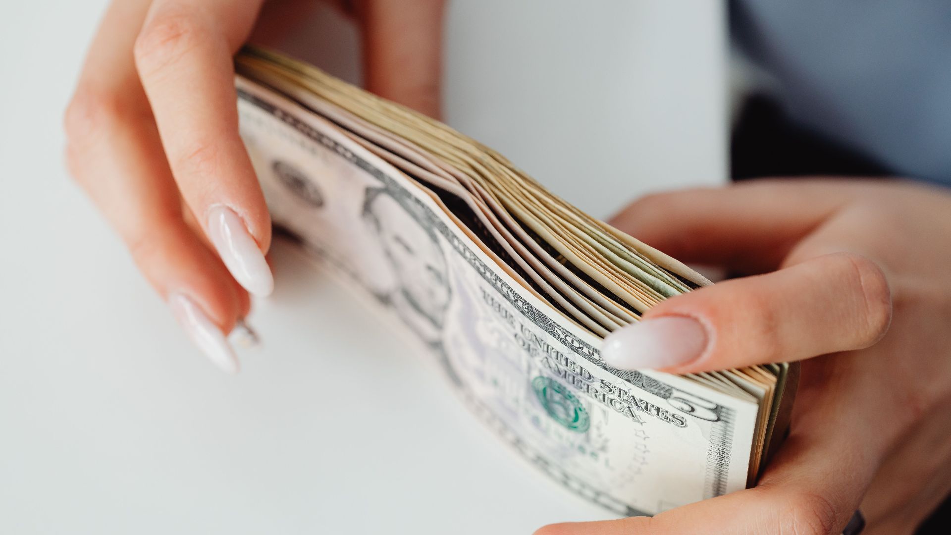 Hands carefully holding a stack of US dollar bills, representing finance and currency.