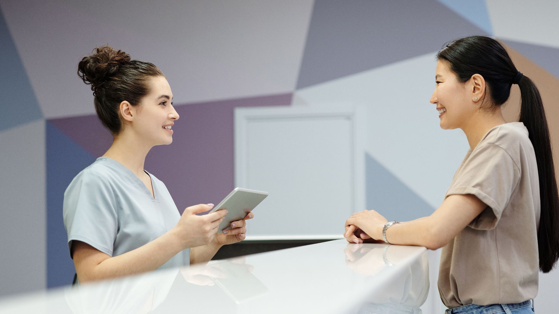 A receptionist and a visitor engaging at a modern reception desk, indoors.
