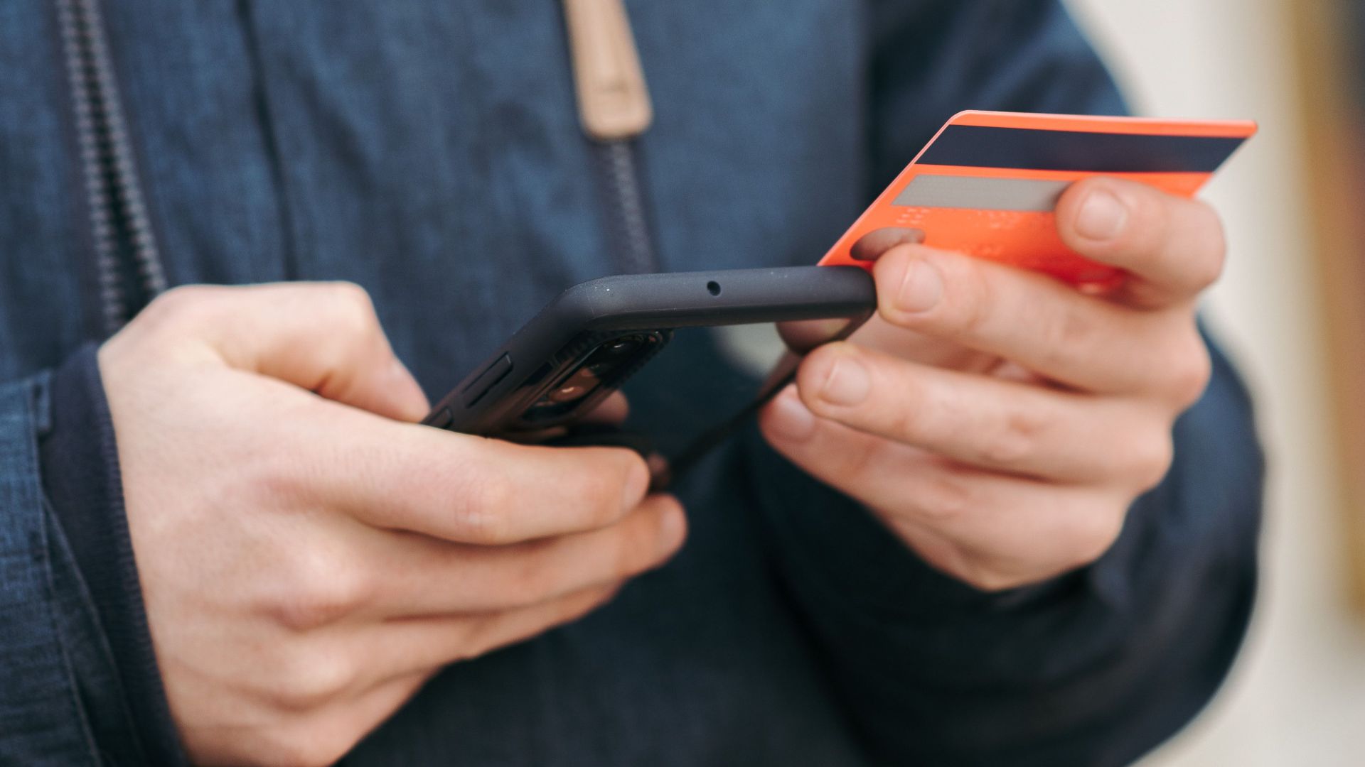 Crop unrecognizable bearded male in warm outerwear entering credit cards details while making online payment via mobile phone on street