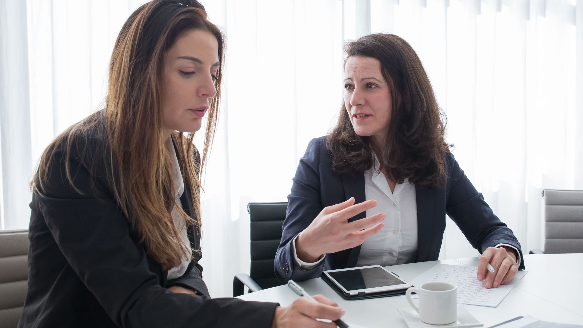 Two women in a business meeting discussing ideas while taking notes.
