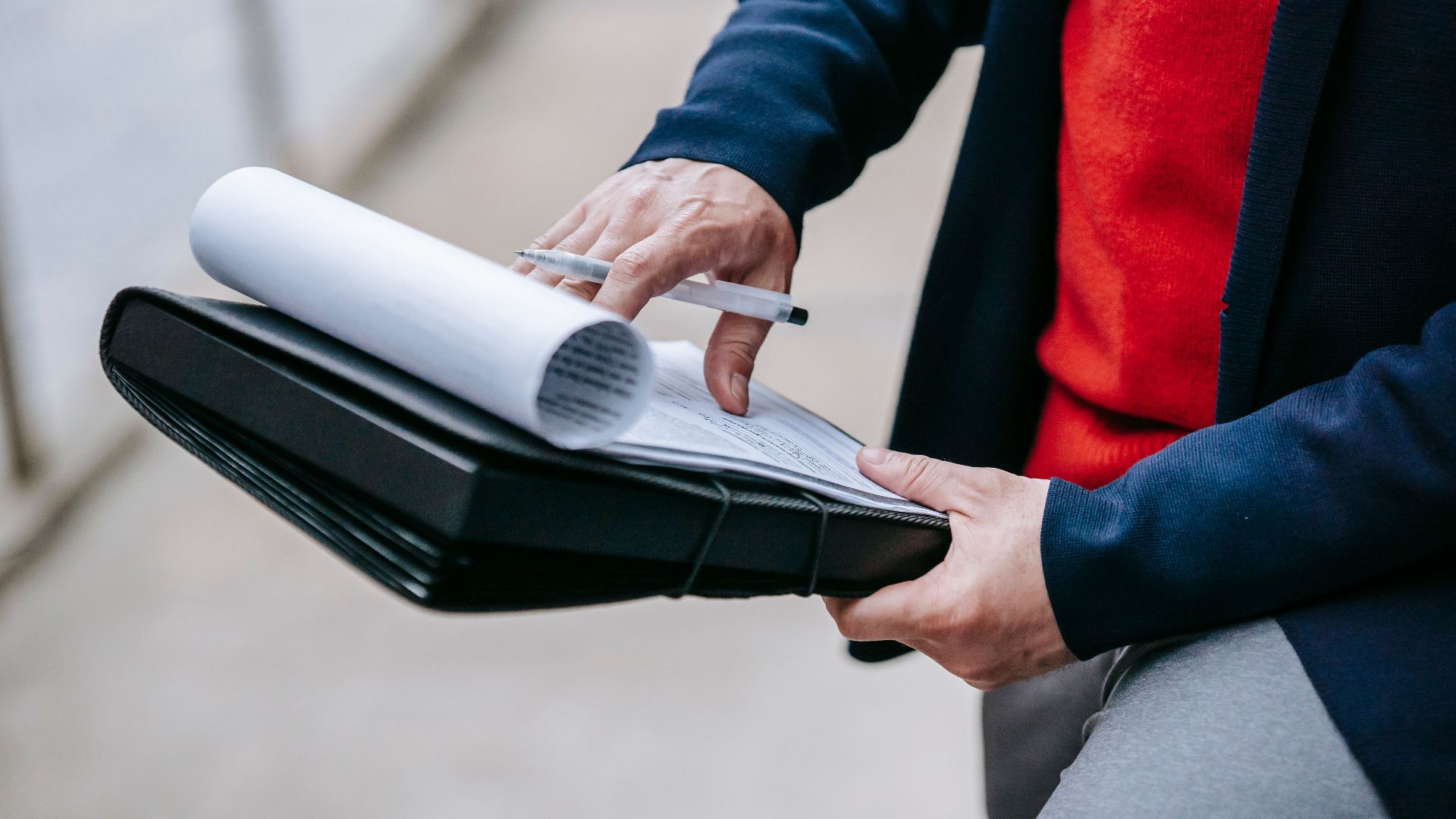 Close-up of a professional person reviewing documents outdoors. Engaged in work with focus on writing materials.