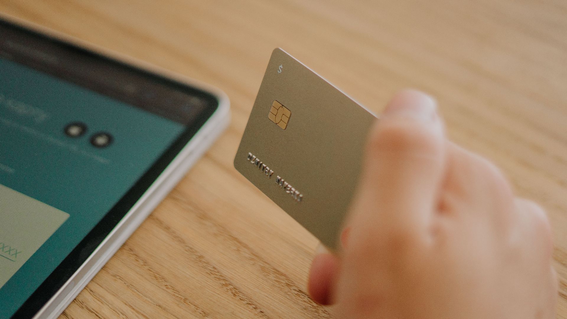 Close-up of a hand holding a credit card near a tablet, depicting online shopping or transaction.