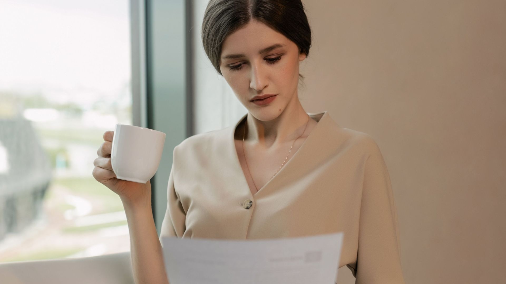 Businesswoman in an office setting reviewing documents while enjoying her coffee.