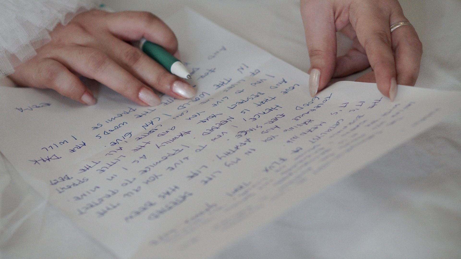 Close-up of a woman's hands writing a handwritten letter with a green pen.
