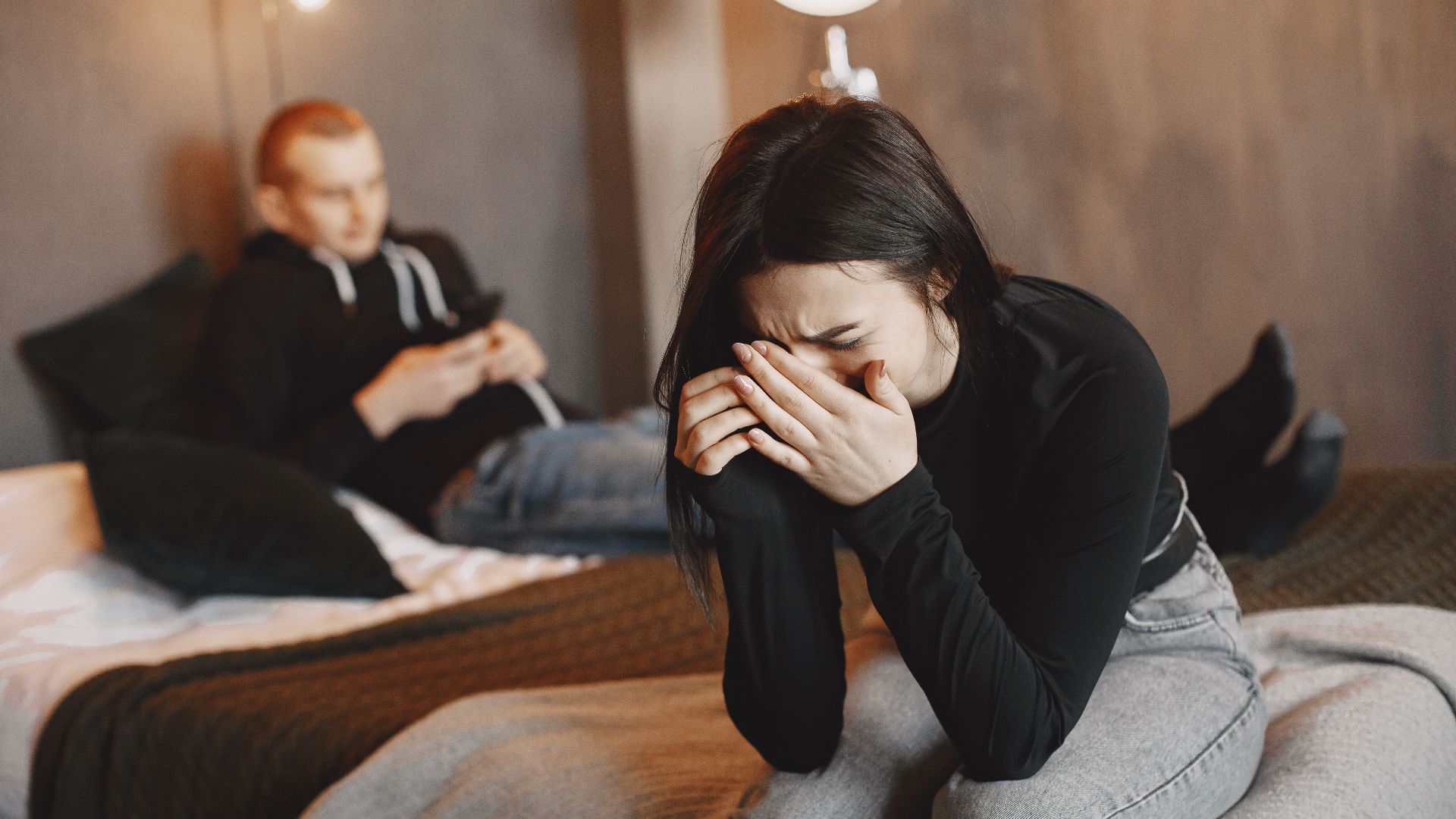 A couple experiencing tension and sadness in a modern bedroom setting.