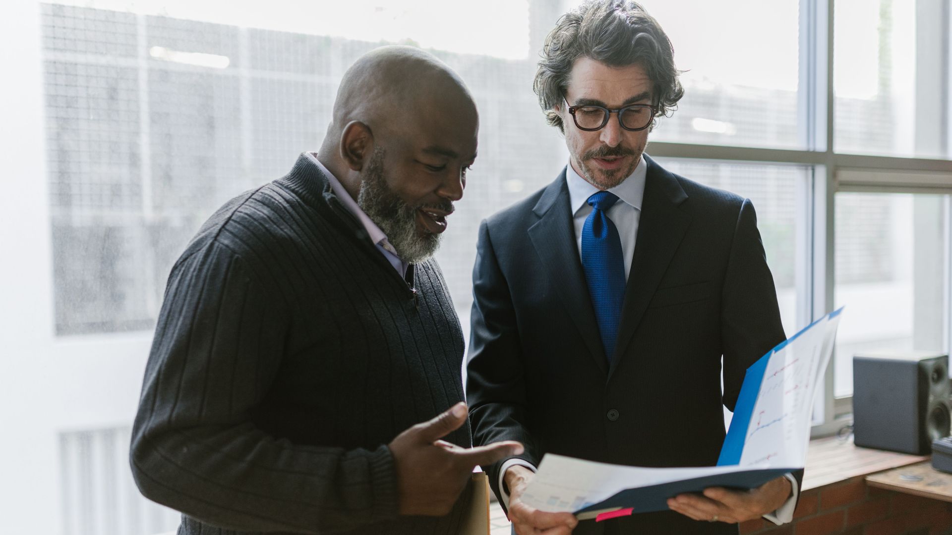 Two businessmen discussing and reviewing documents in a modern office setting.