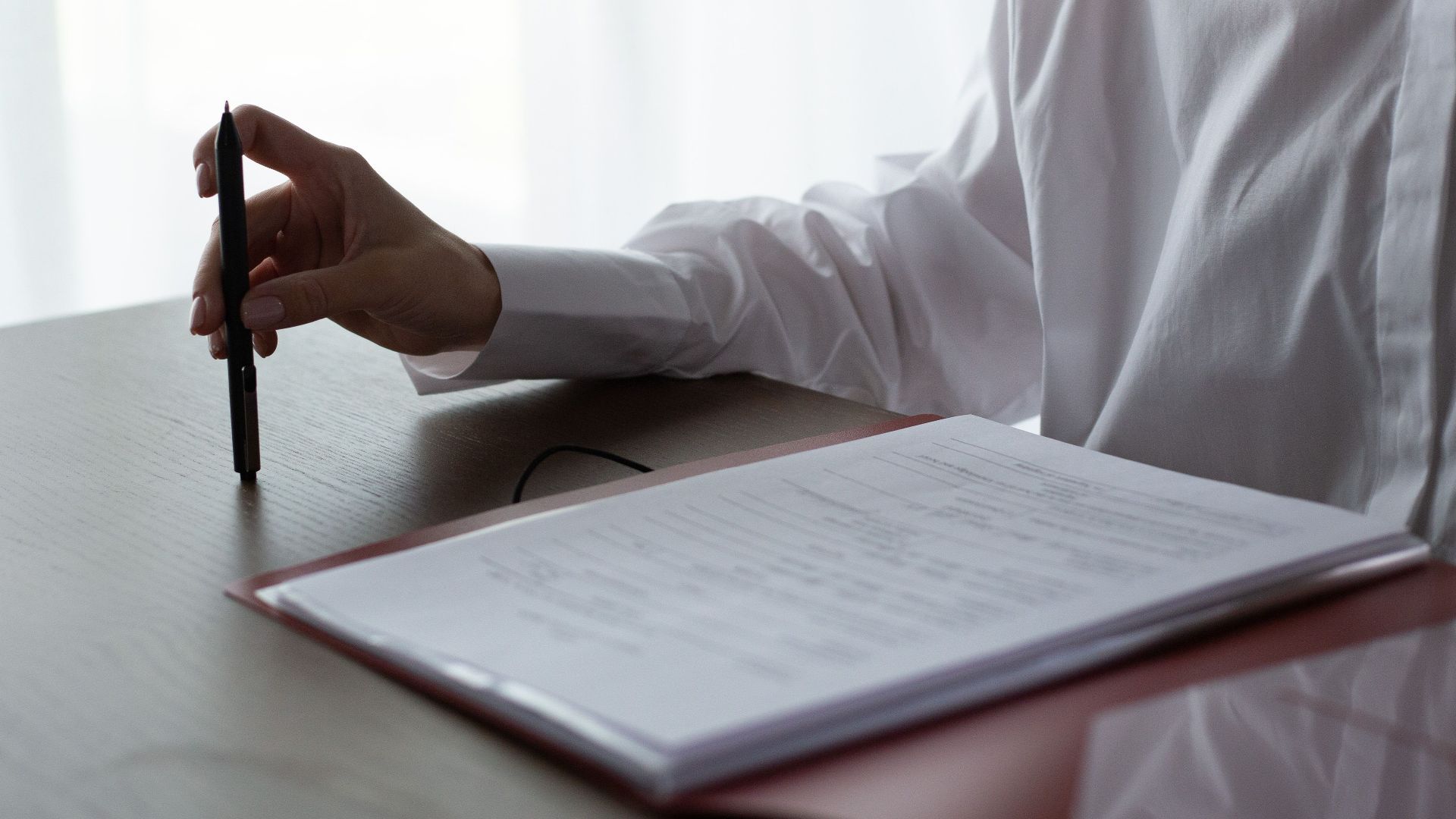 A woman examines documents, holding a pen over a table in a bright indoor setting.