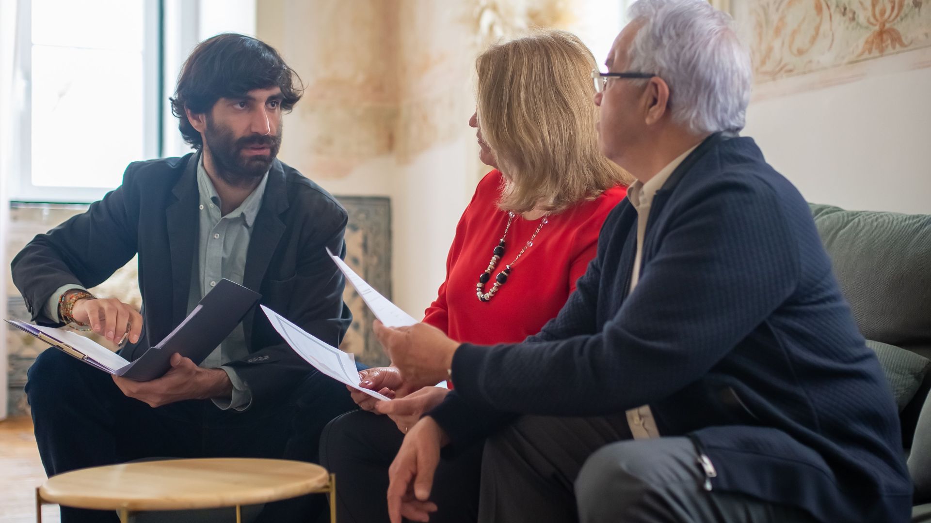 An advisor discussing financial documents with a senior couple indoors in a cozy living room setting.