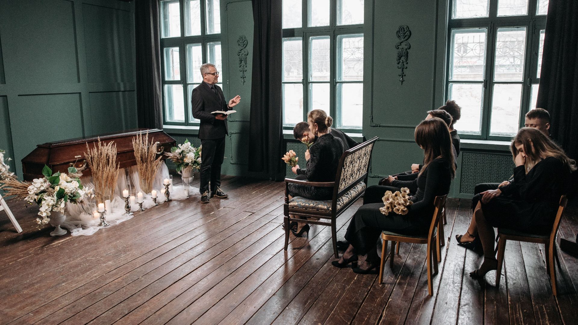 A solemn funeral ceremony indoors with family and officiant present.