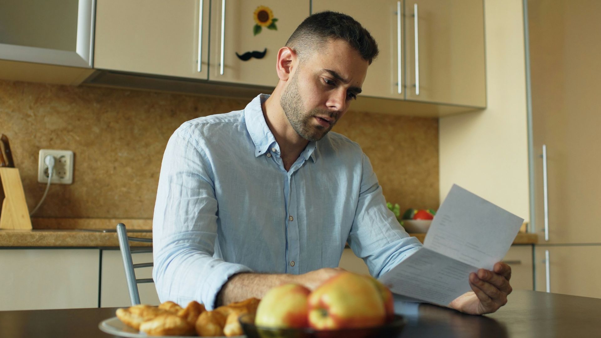 Man reading document at kitchen table with fruit and fruit