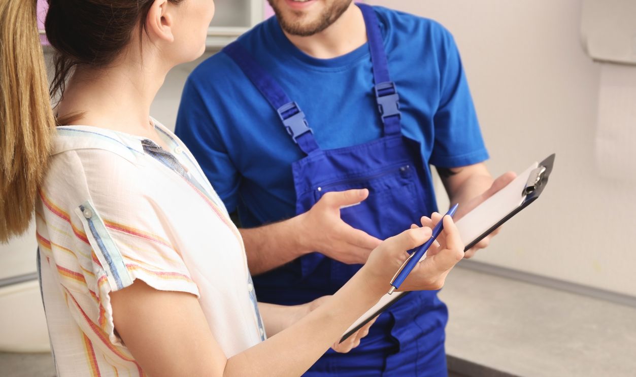 Professional plumber in uniform talking to client indoors