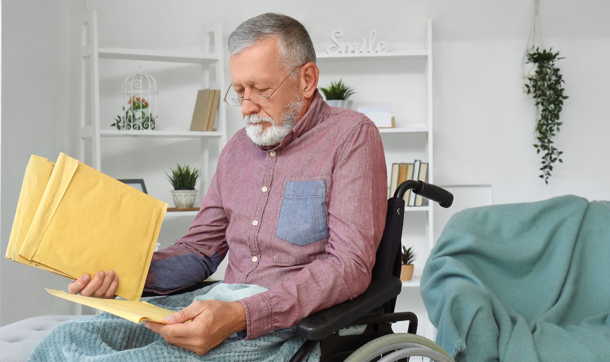 Senior man in wheelchair and with envelopes at home