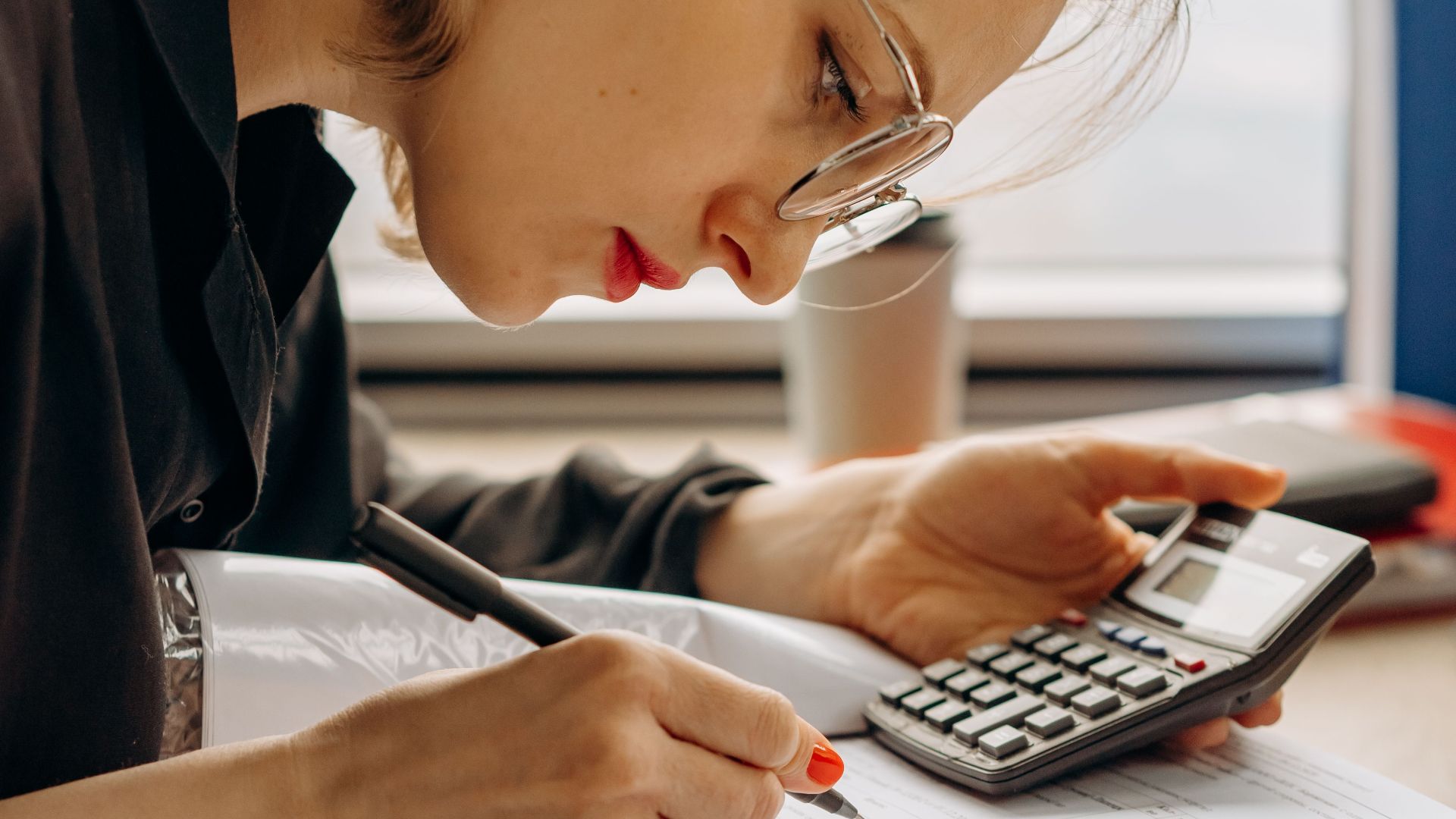 Woman with eyeglasses concentrating on financial calculations with notebook and calculator.