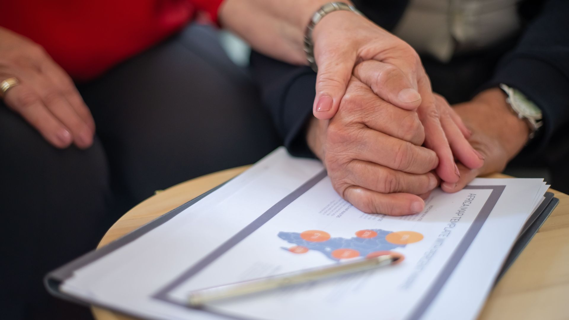 Two adults holding hands over business documents, symbolizing support and partnership.