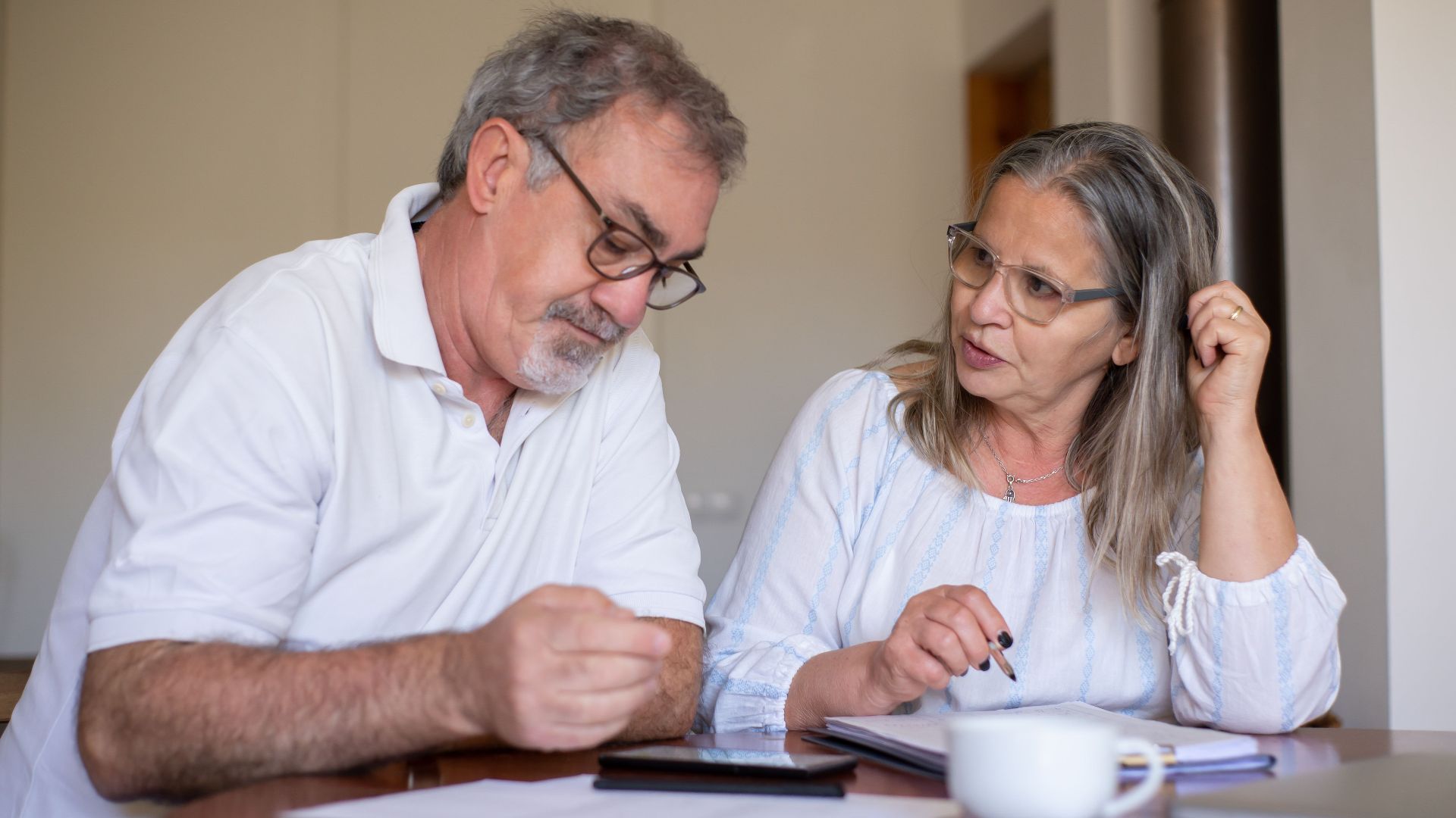 Senior couple reviewing documents and managing finances together at home, showing collaboration and care.