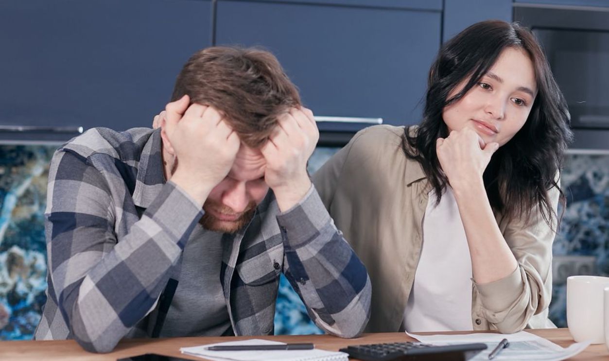 A couple looking worried while reviewing financial documents at a kitchen table
