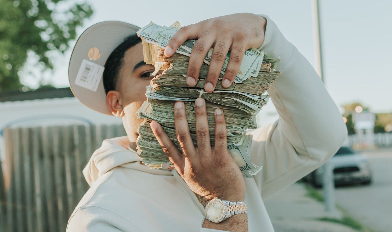 Man wearing a hoodie and analog watch holding stack of cash outdoors in Omaha, NE.