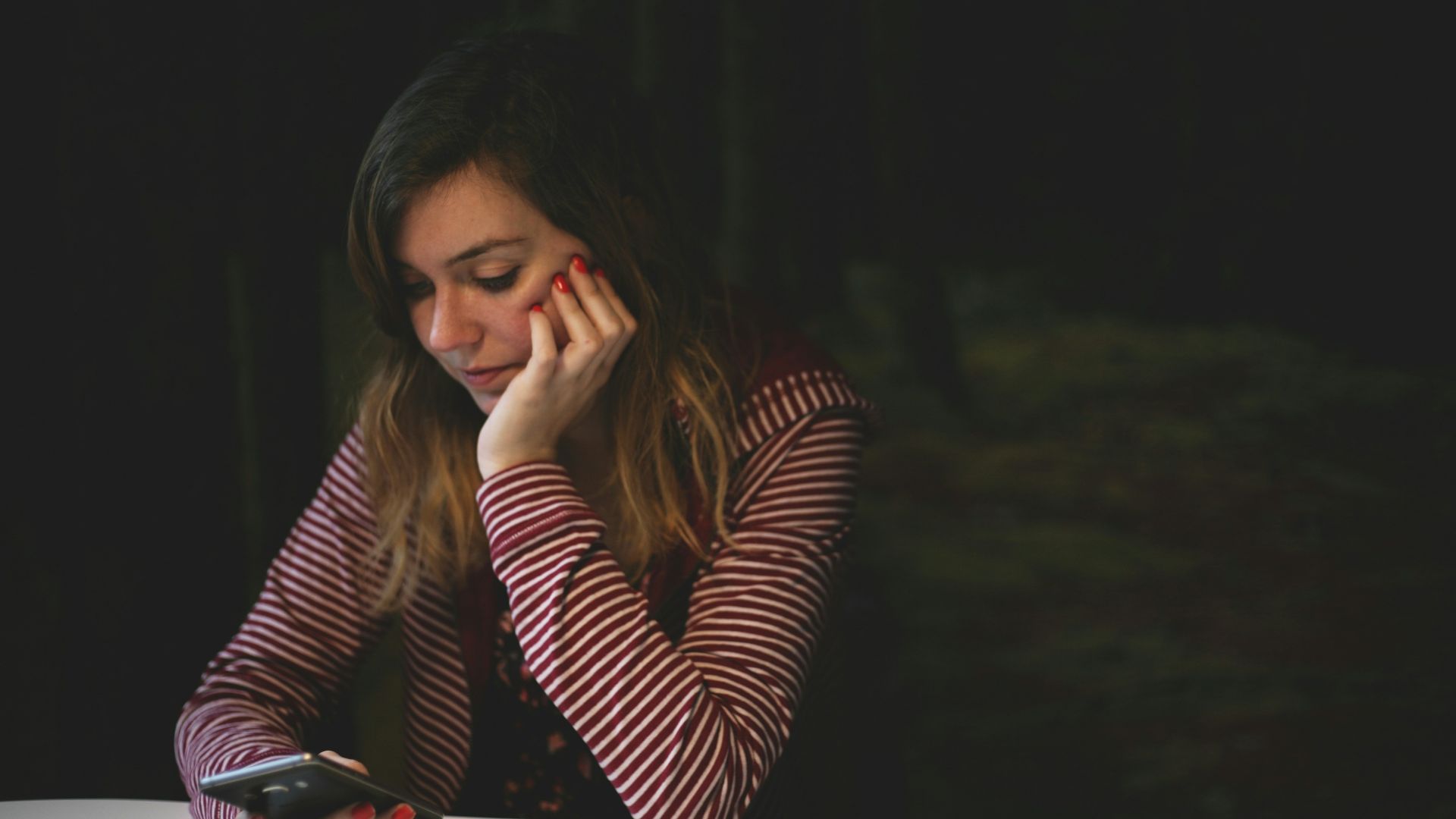 woman leaning on white wooden table while holding black Android smartphone