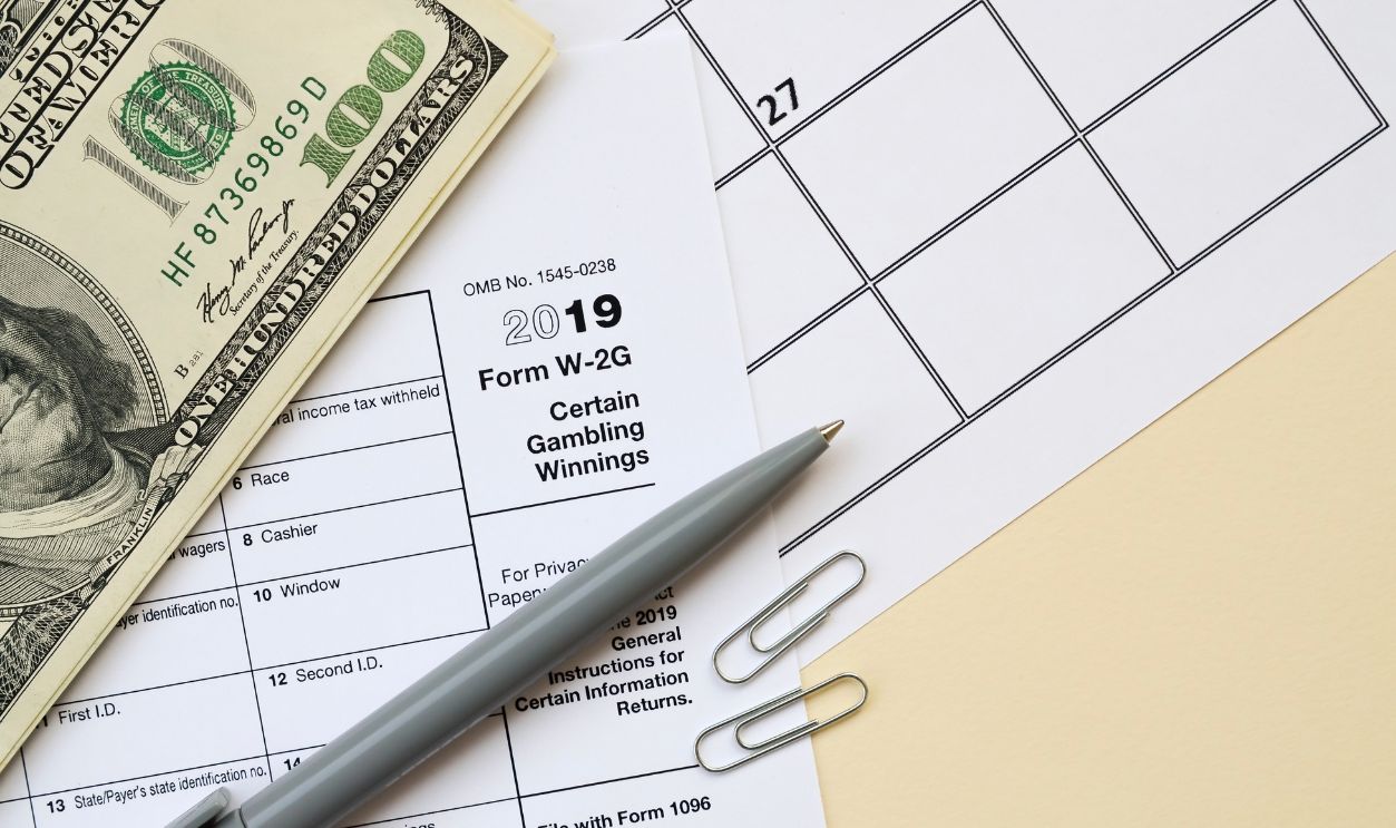 IRS Form W-2G Certain Gambling Winning blank lies with pen and many hundred dollar bills on calendar page