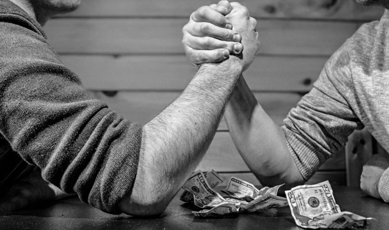 Two men engage in a high-stakes arm wrestling match surrounded by money on a table