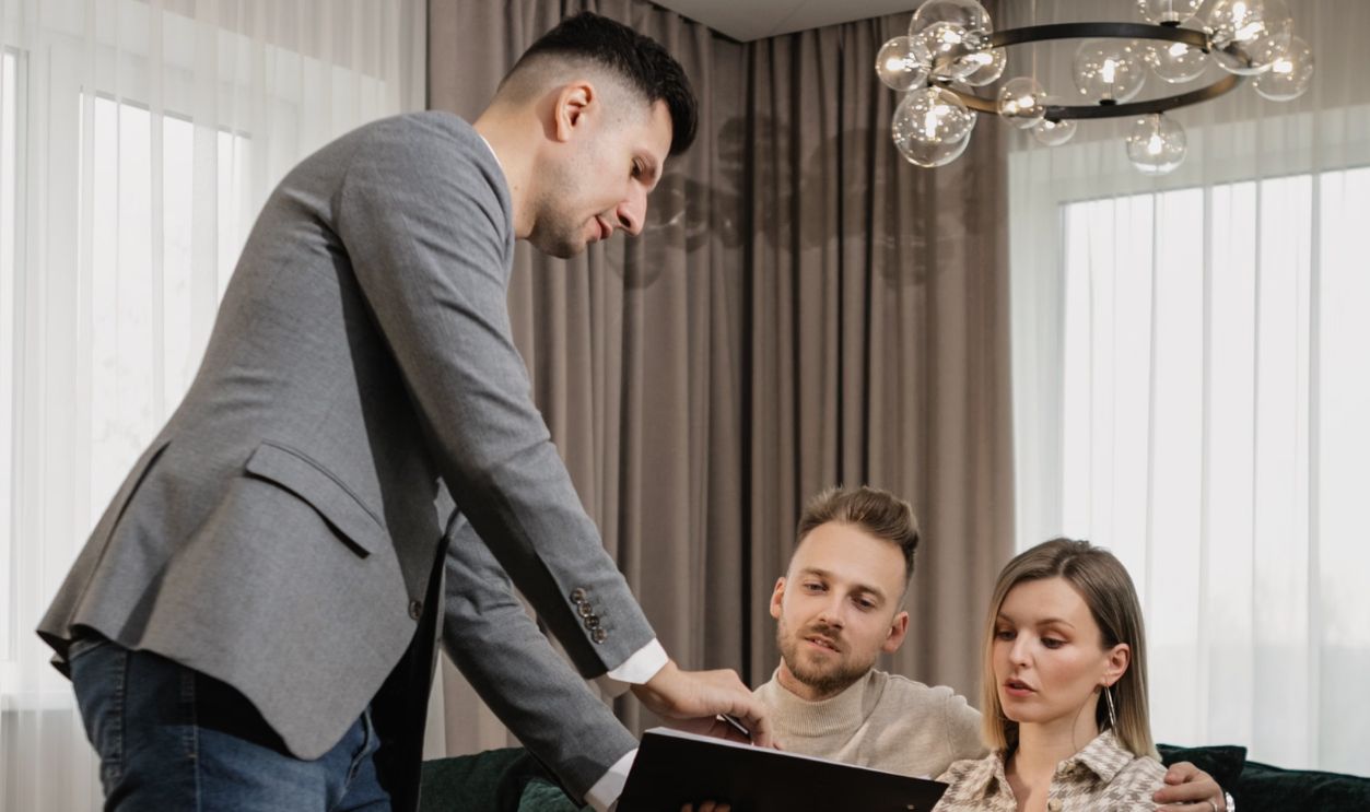 A real estate agent shows a document to an attentive couple seated on a sofa, indoors